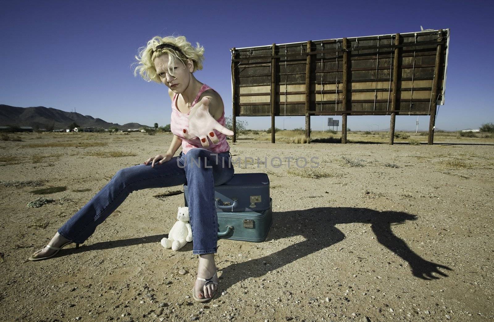 Woman sitting on suitcases in front of an old billboard reaching to the camera