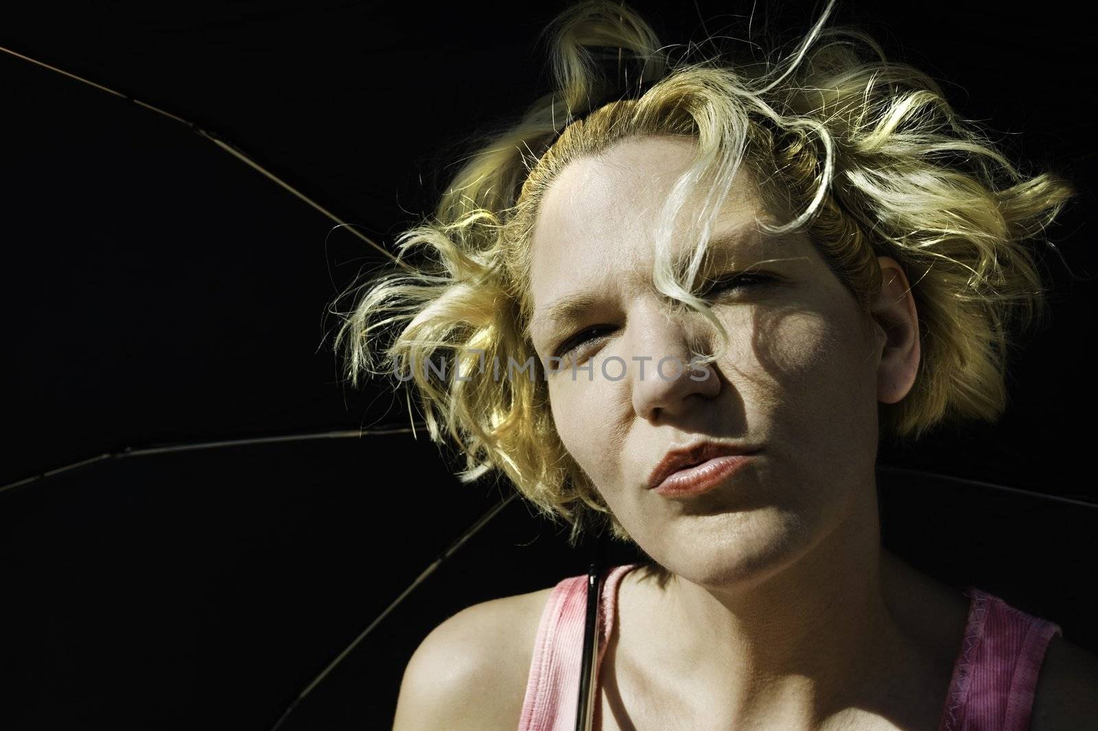 Blonde woman with crazy hair under a black umbrella