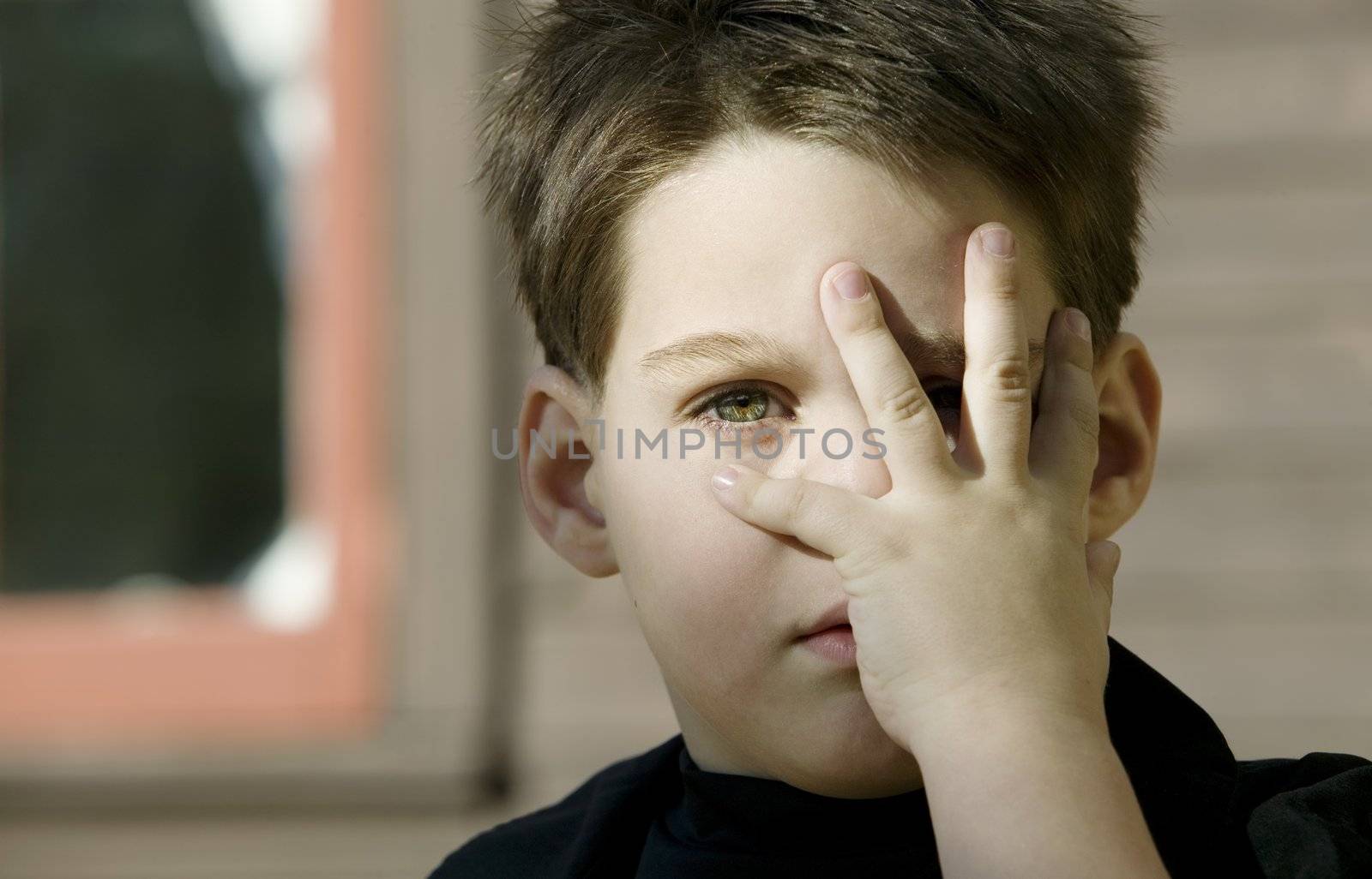 Close up of a young boy with his hand covering one eye.