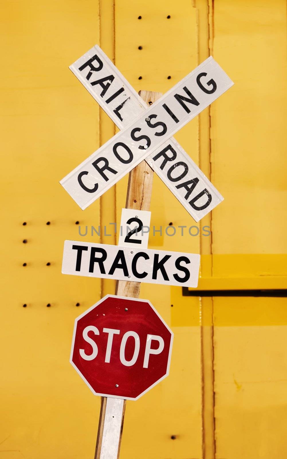 Railroad crossing stop sign against a yellow train car.