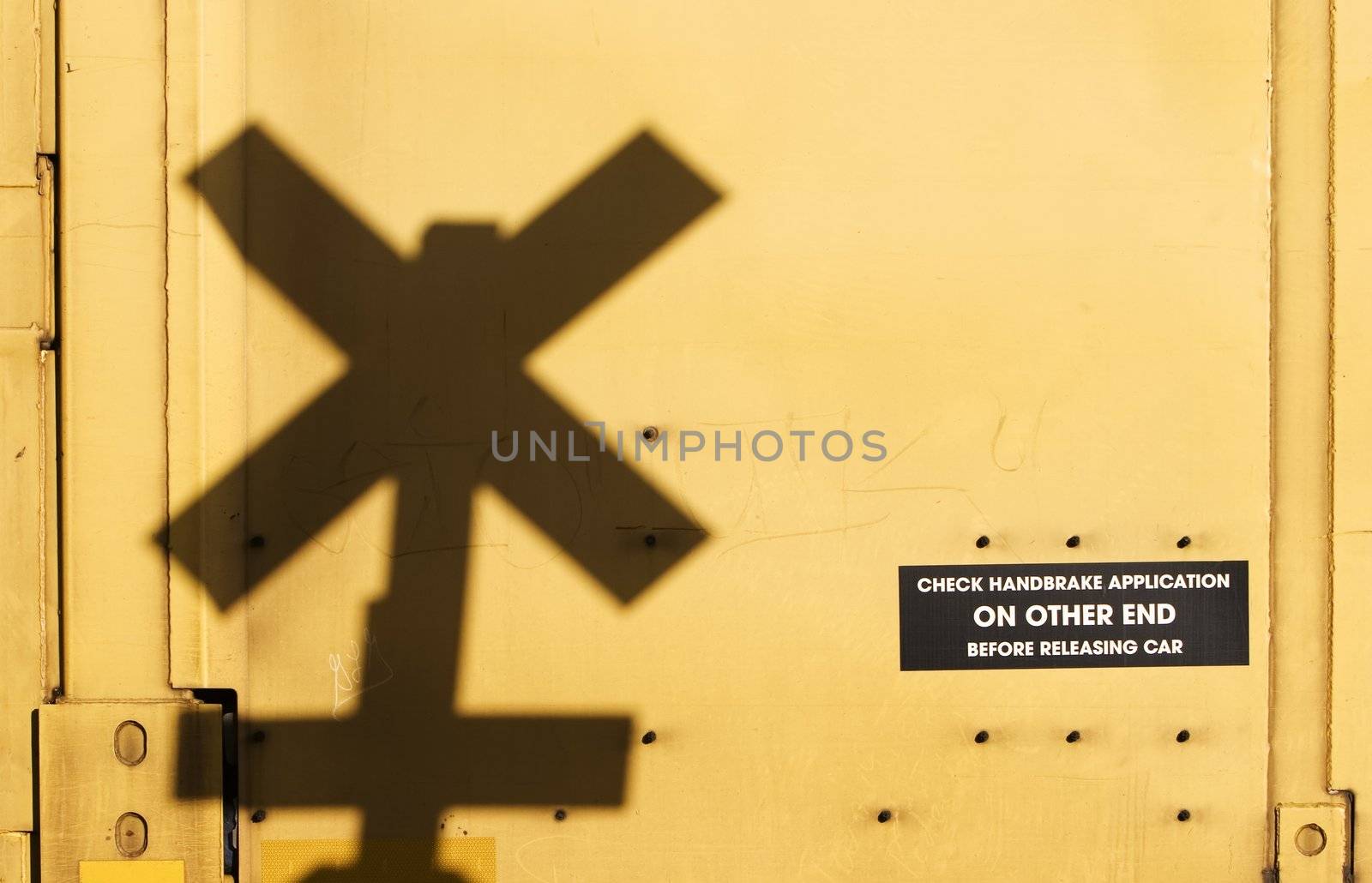 Shadow of a railroad crossing sign cast against the yellow side of a freight train car.
