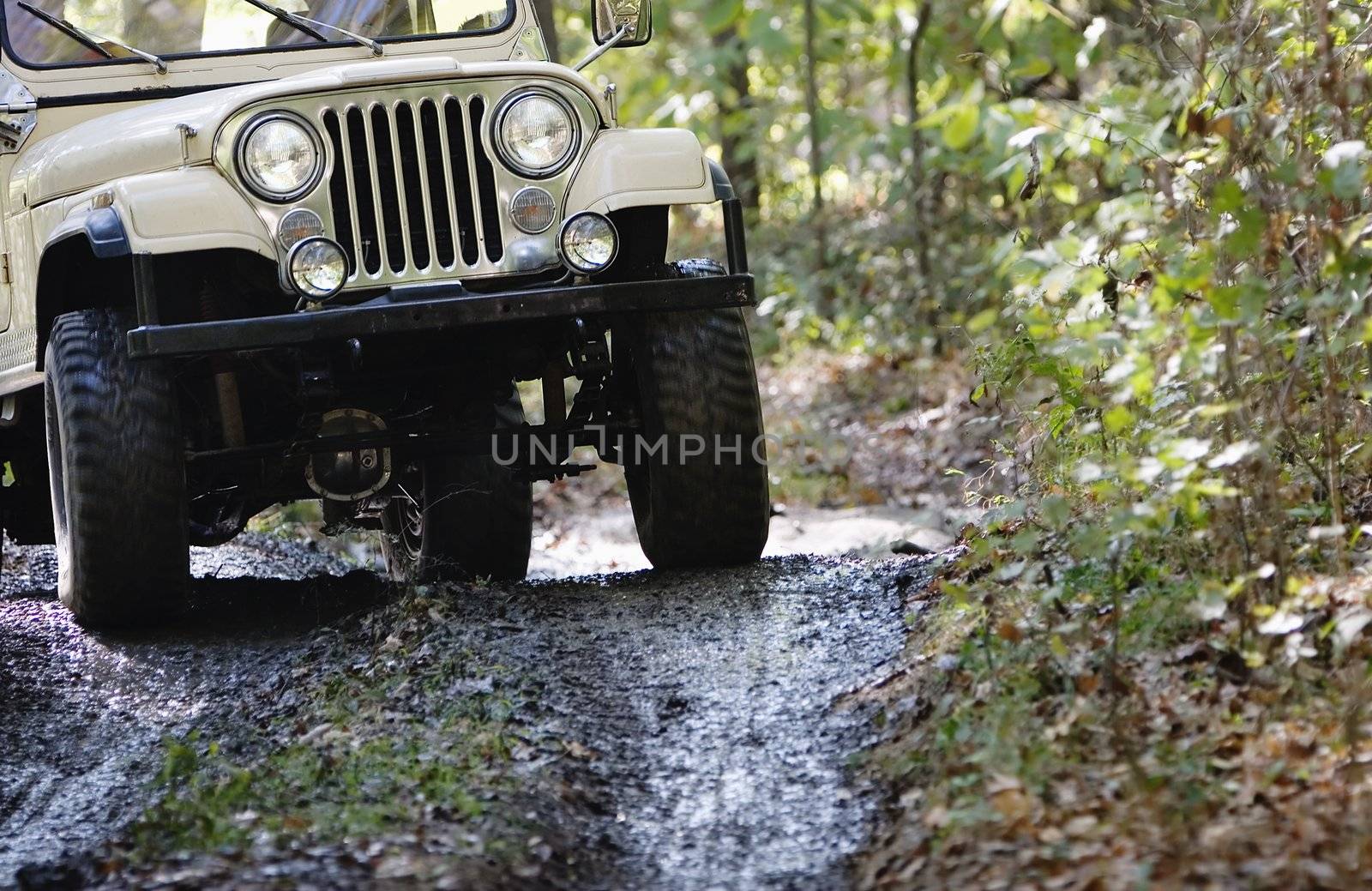 Headlights and grille on a vintage four-wheel drive vehicle driving in the mud.