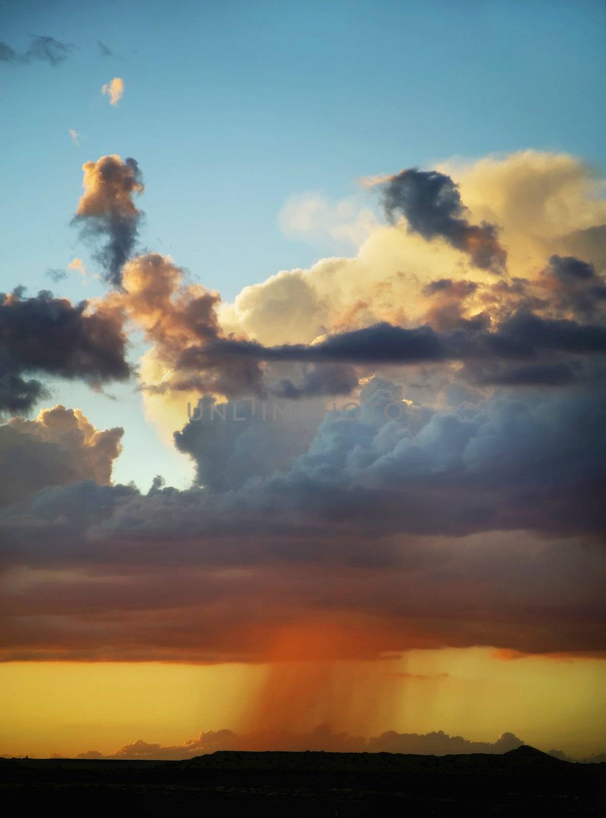 A distance rain cloud at sunset underneath a blue sky.