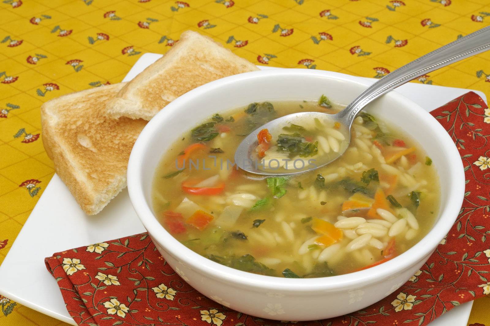 Vegetable soup with pasta served with bread slices on a colorful tablecloth