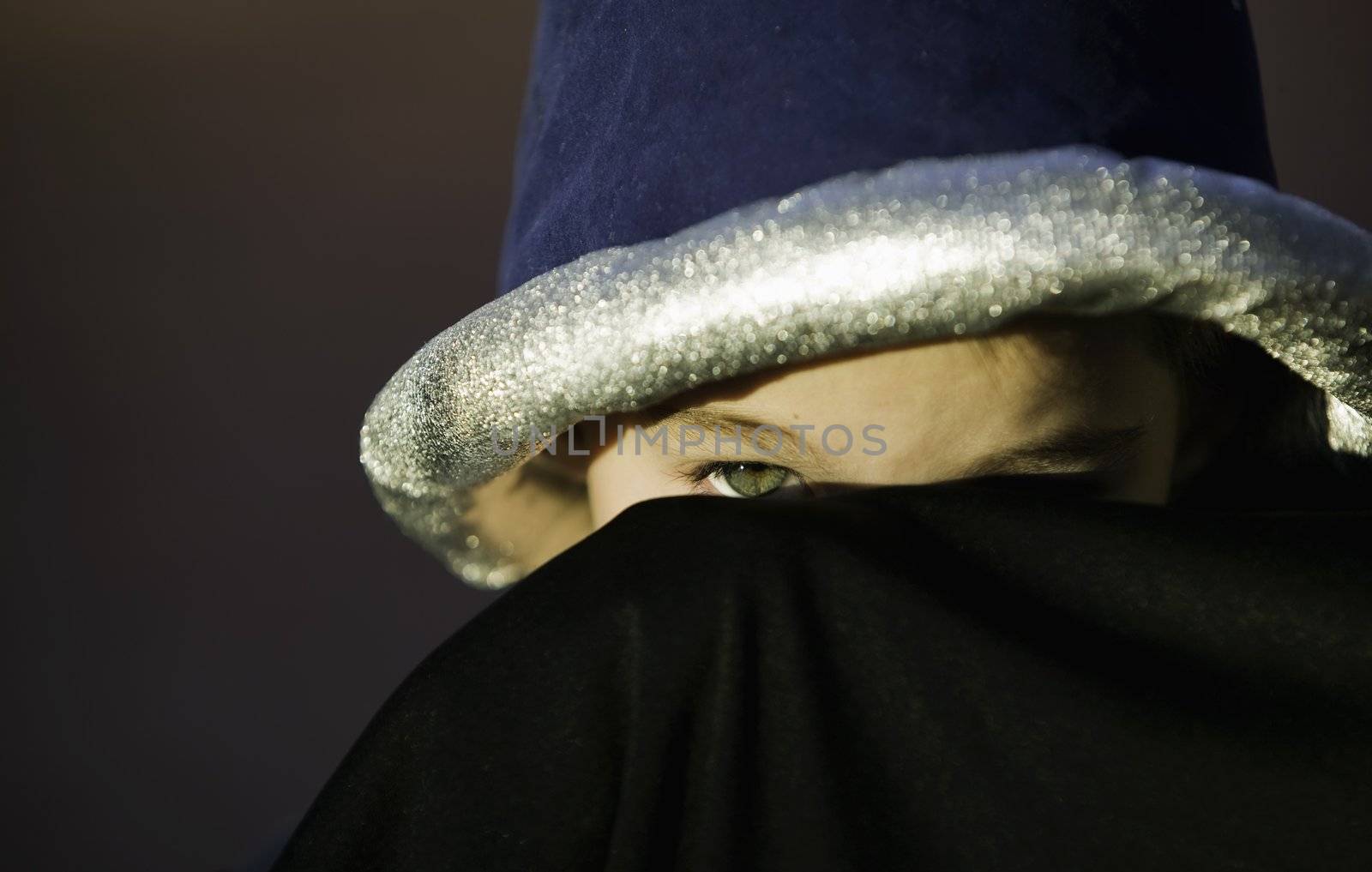 Young boy peeks out from underneath a costume sorcerer hat