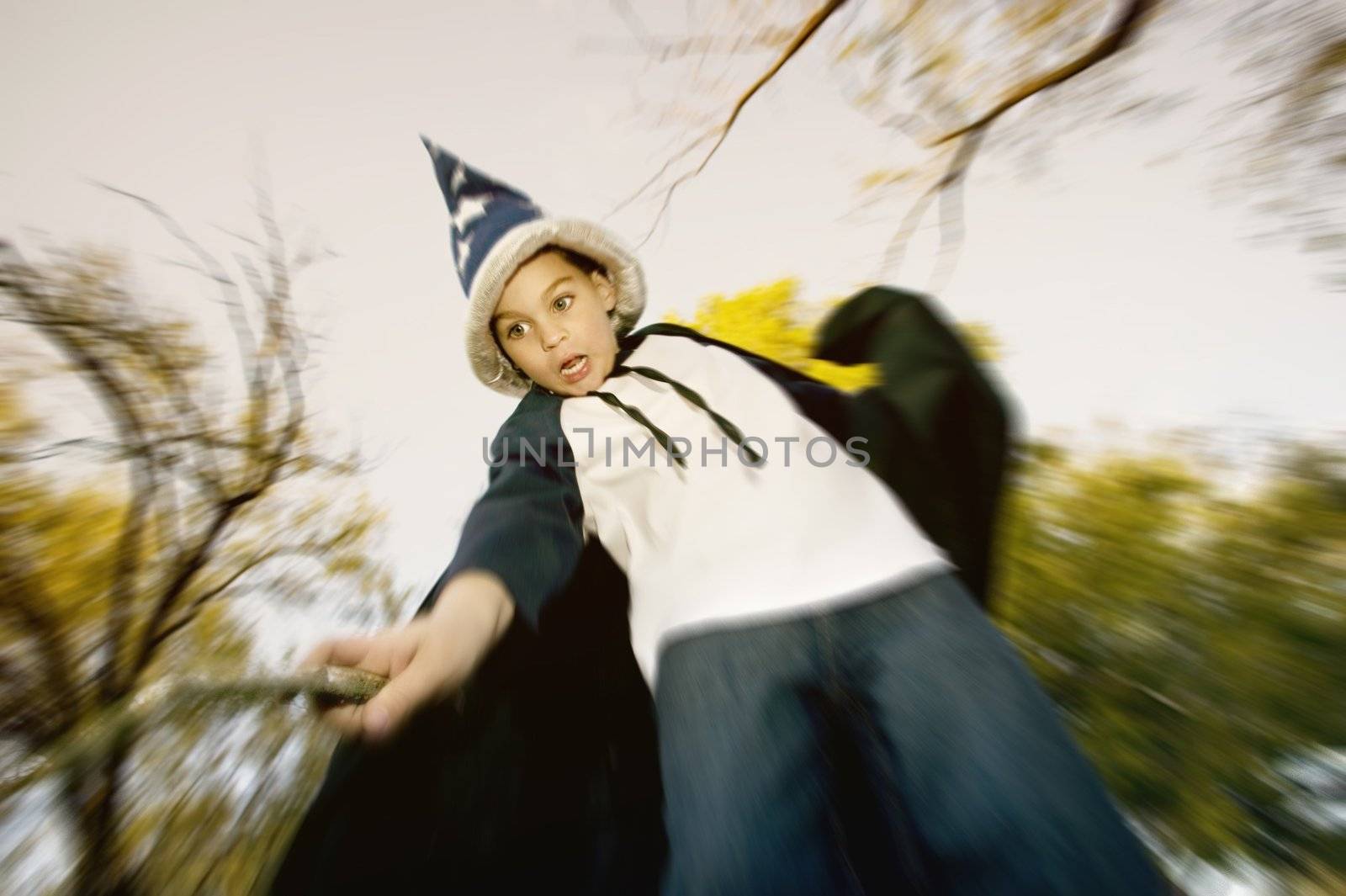 Young boy in a wizard costume casts a spell with a stick wand.