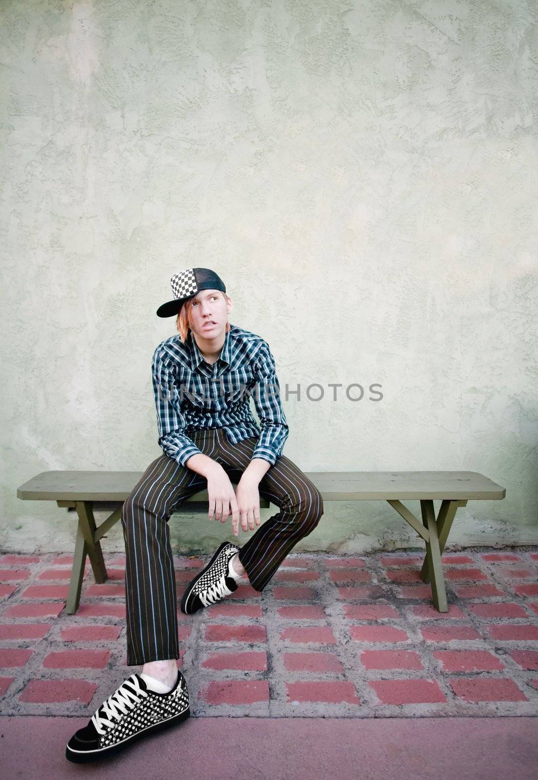 Teenage boy sitting on a green bench in front of a stucco wall