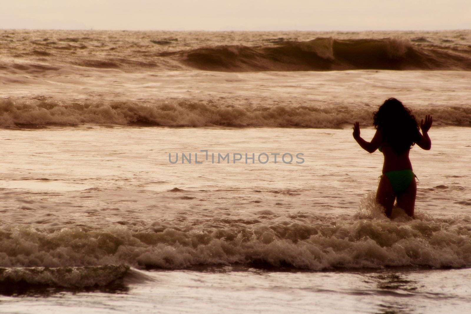 A woman in silhouette heads out into the ocean.