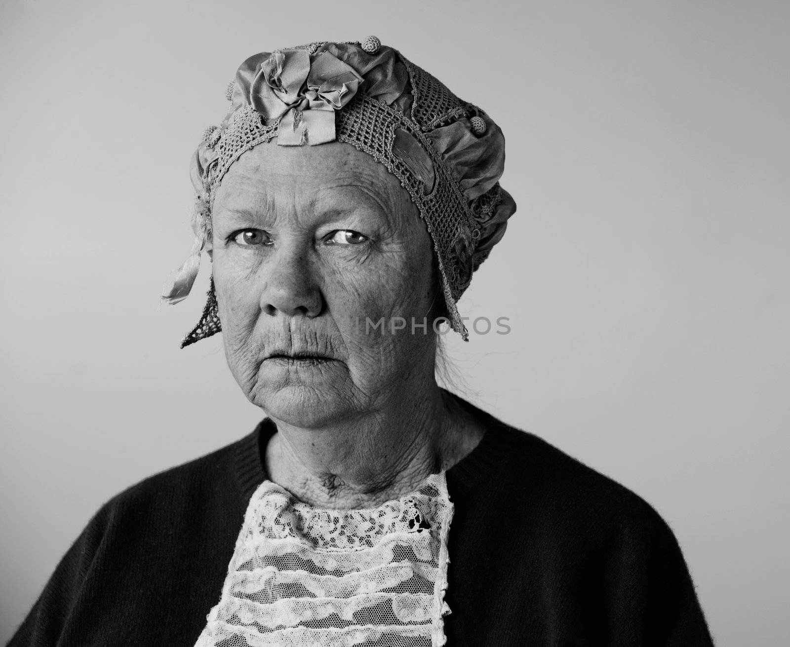 Dour senior woman in the studio wearing a vintage hat and lace.