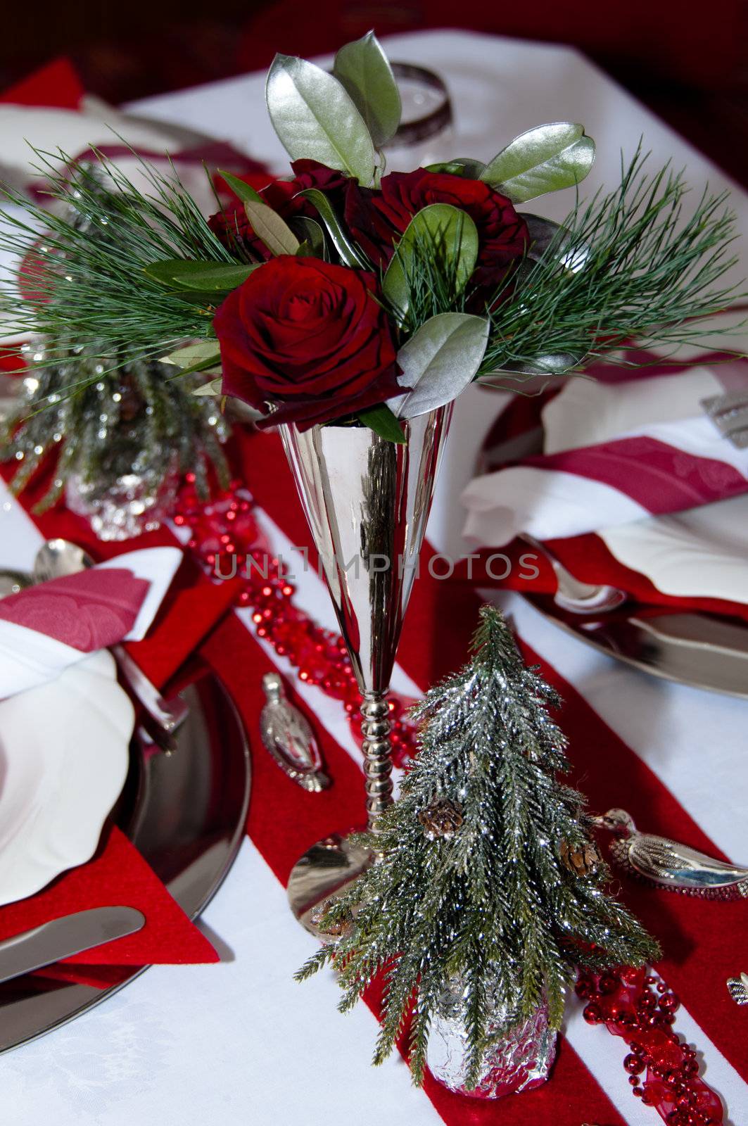 Christmas table with red decoration, napkins, roses, silver, christmas tree and candles