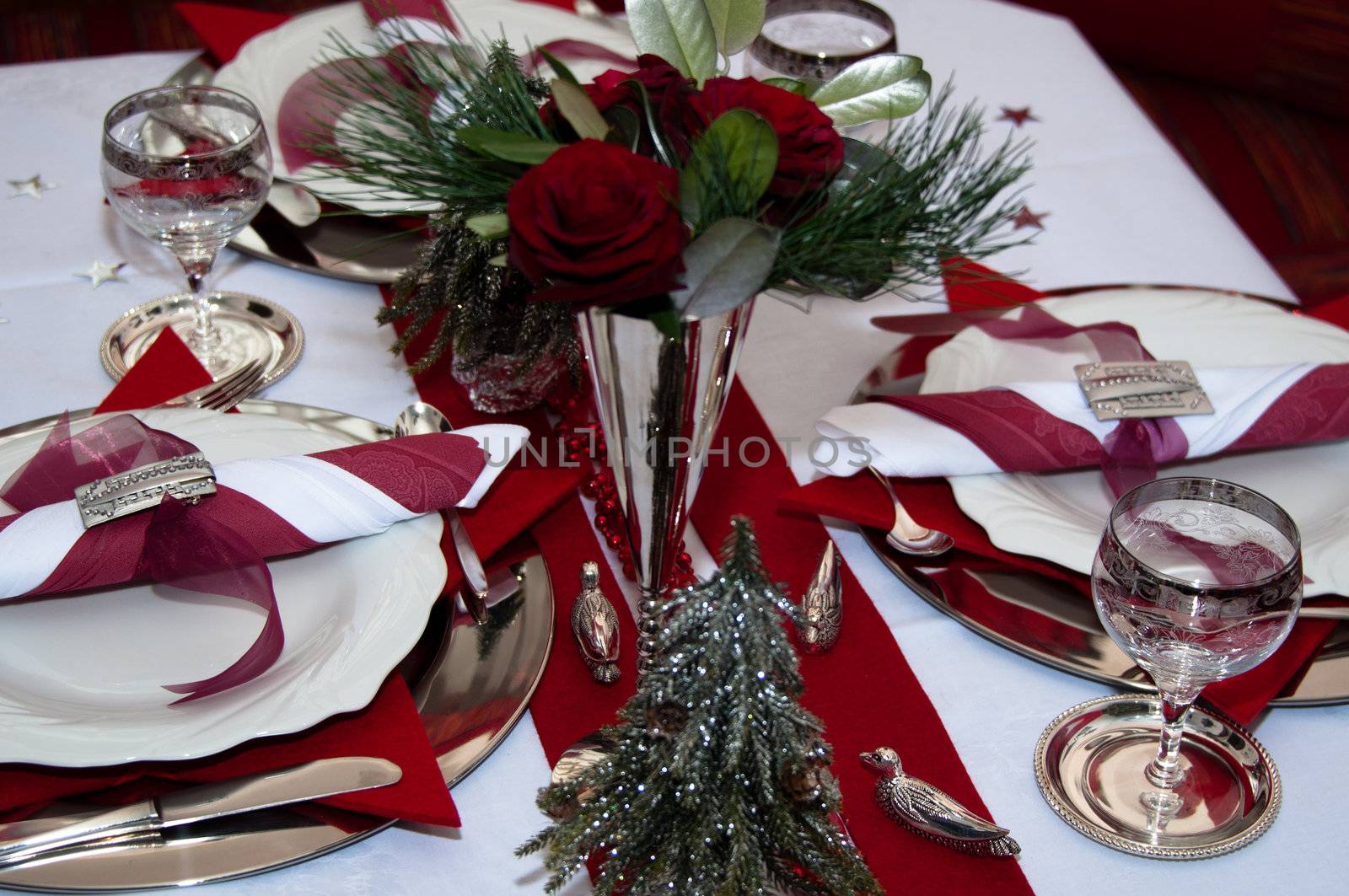 Christmas table with red decoration, napkins, roses, silver, christmas tree and candles