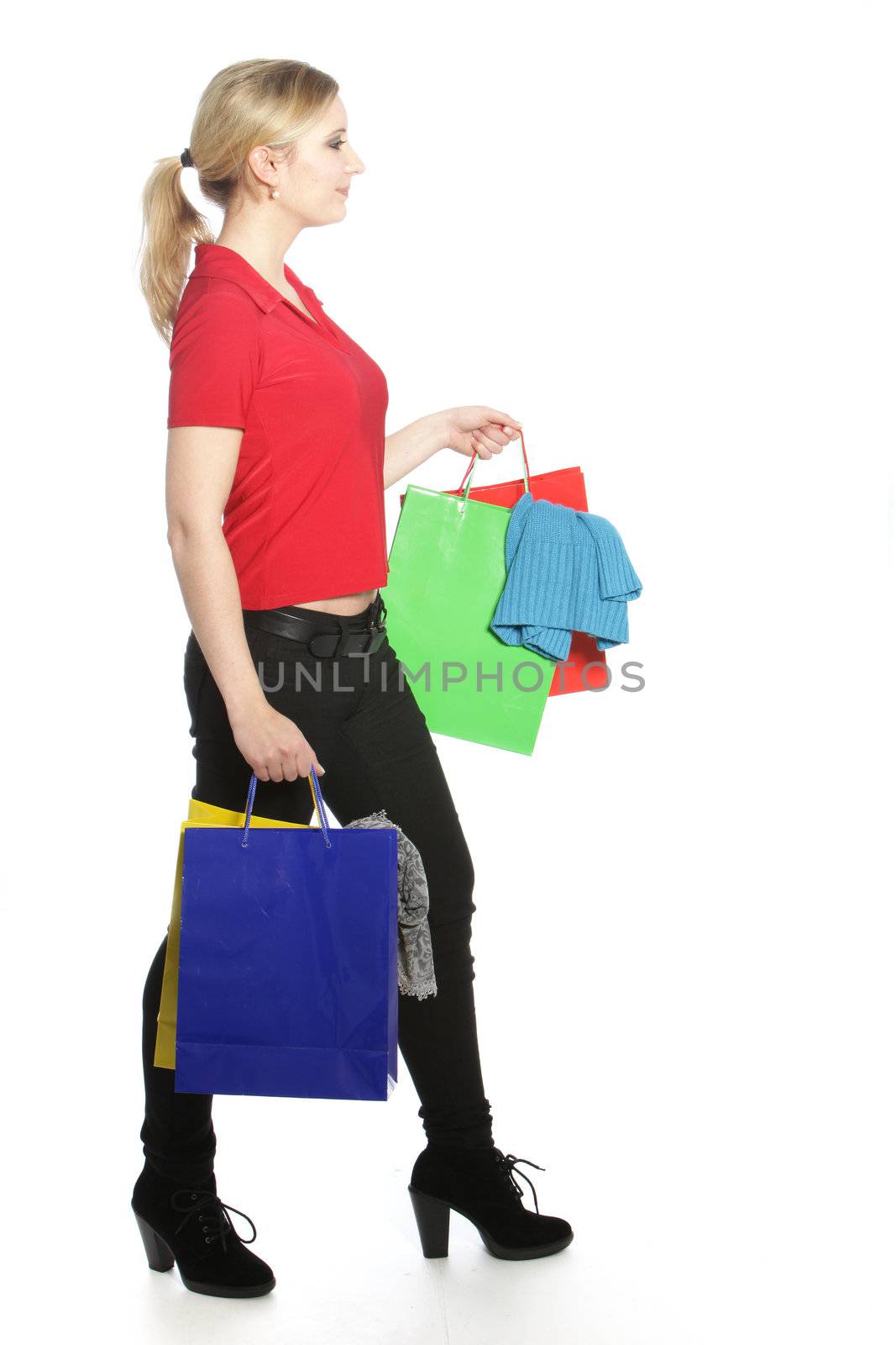 Happy attractive trendy woman shopper walking along with her hands full of purchases in multiple colourful shopping or carrier bags isolated on white