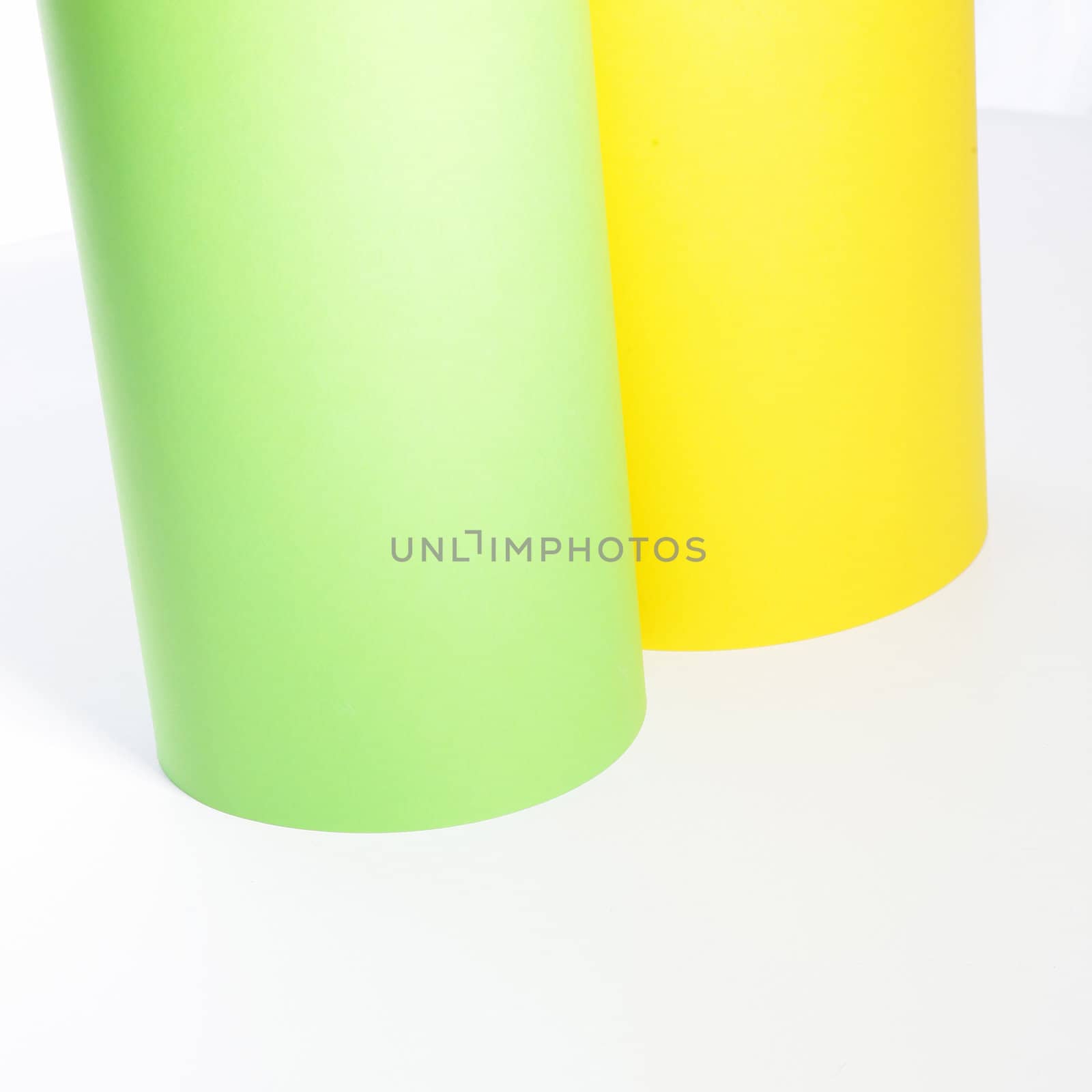 Green and yellow rolls of cardboard standing upright alongside each other on a white background with copyspace