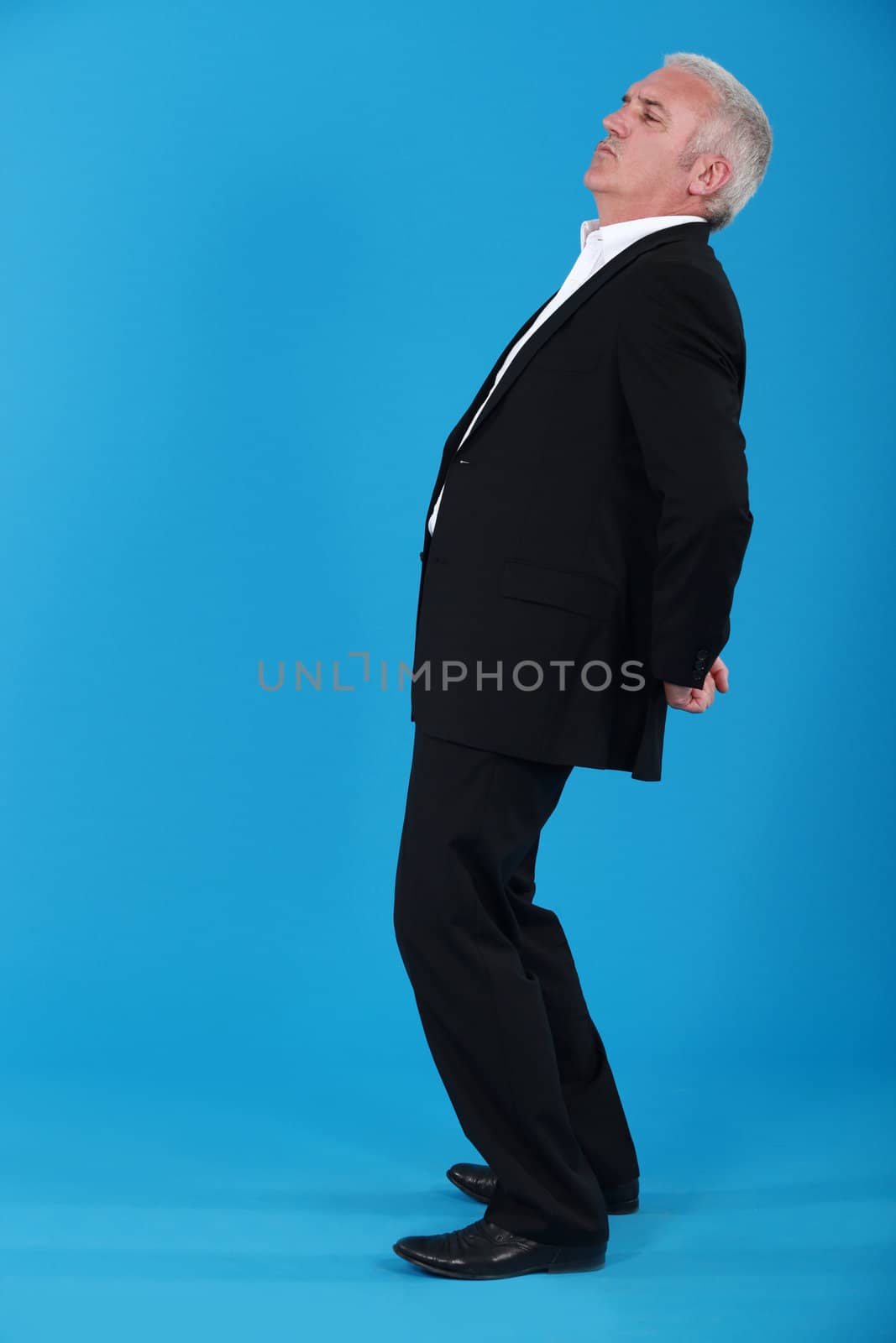portrait of mature man standing back in profile against blue background by phovoir