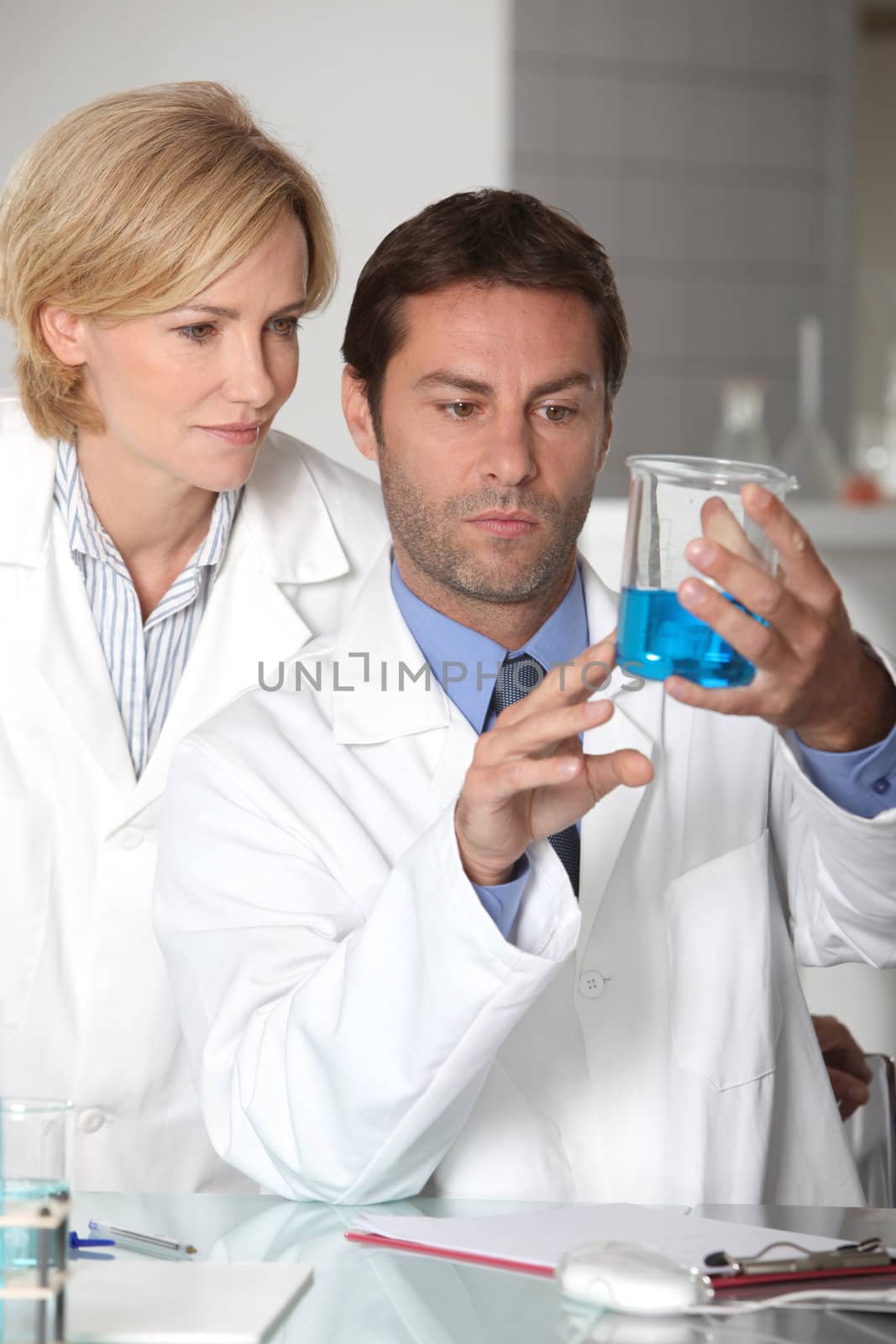 Man and woman in white laboratory coats, examining blue liquid by phovoir