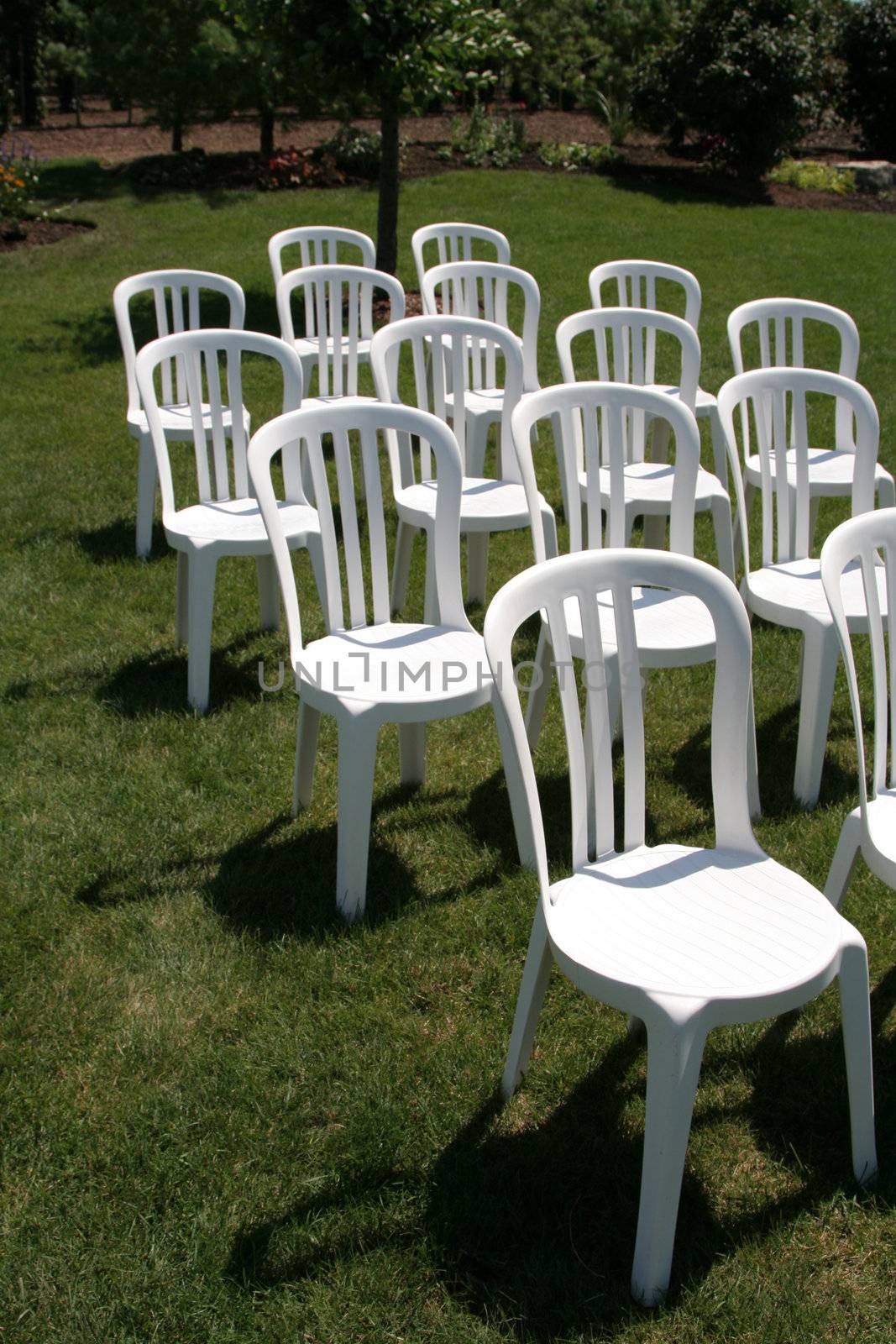 A bunch of whit plastic chairs organized on green grass.