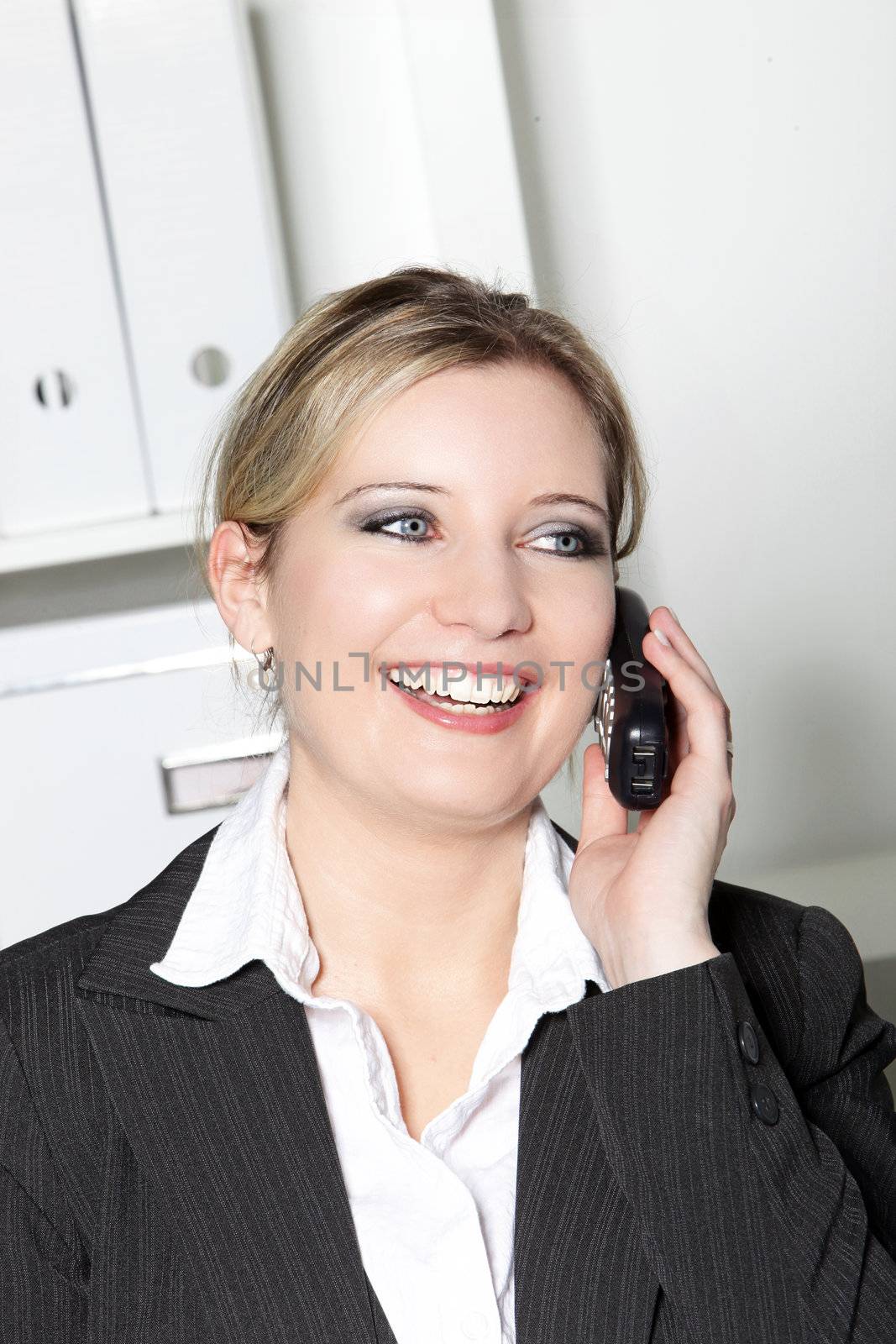 Happy stylish attractive businesswoman with a beautiful wide smile talking on a mobile phone in her office