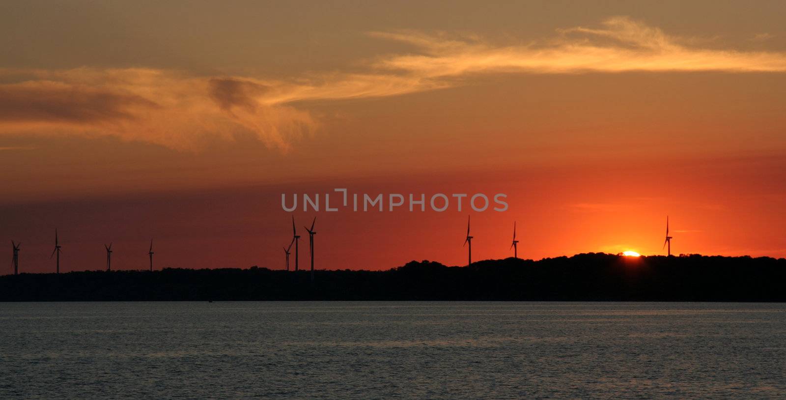 The sun setting just over the horizon with wind turbines in the background.