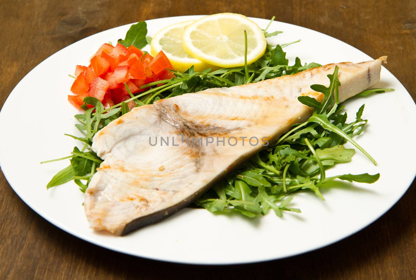 roasted swordfish with lemon, salad and tomatoes on wooden background