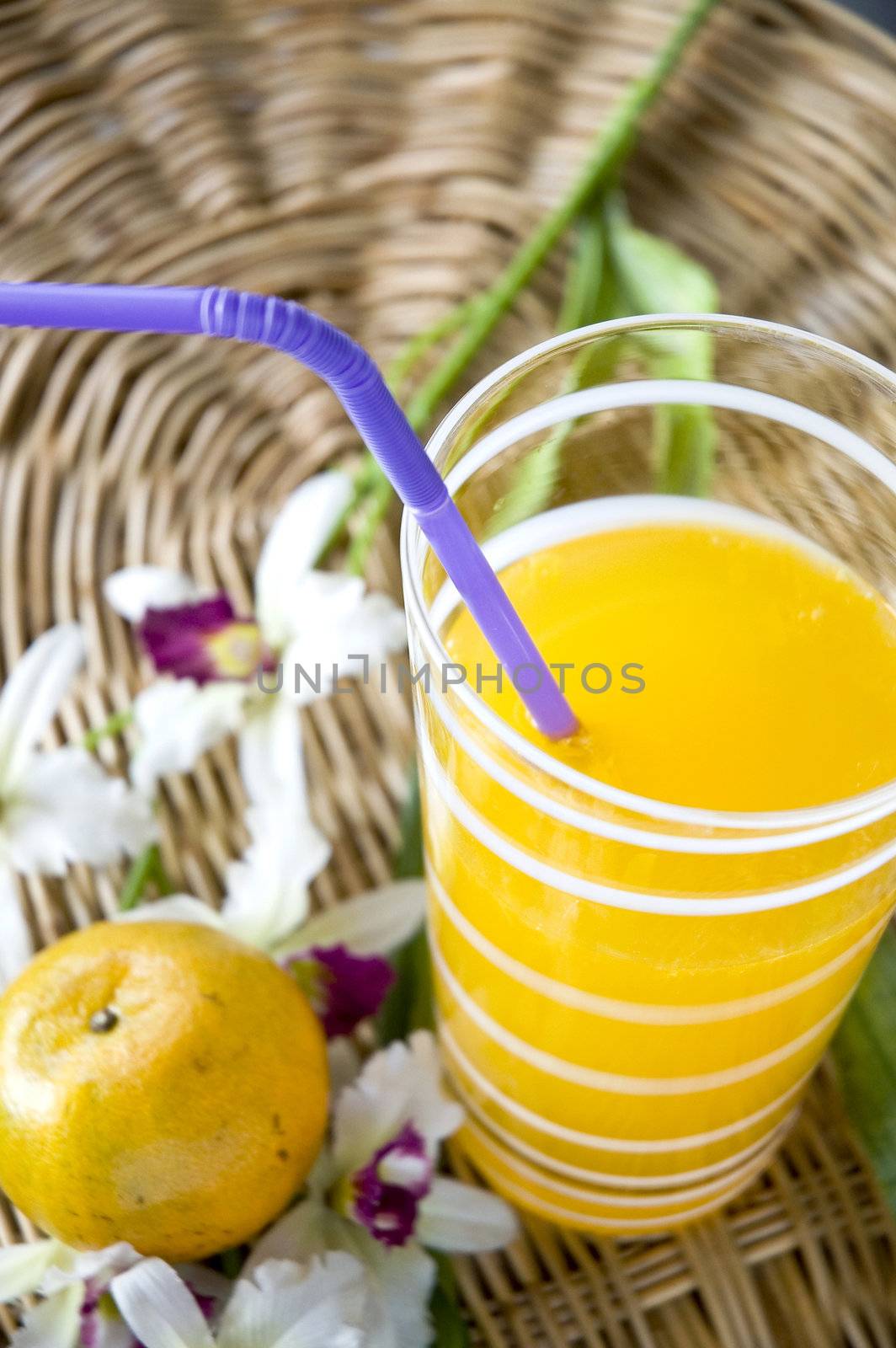 glass of juice put beside an orange and orchid