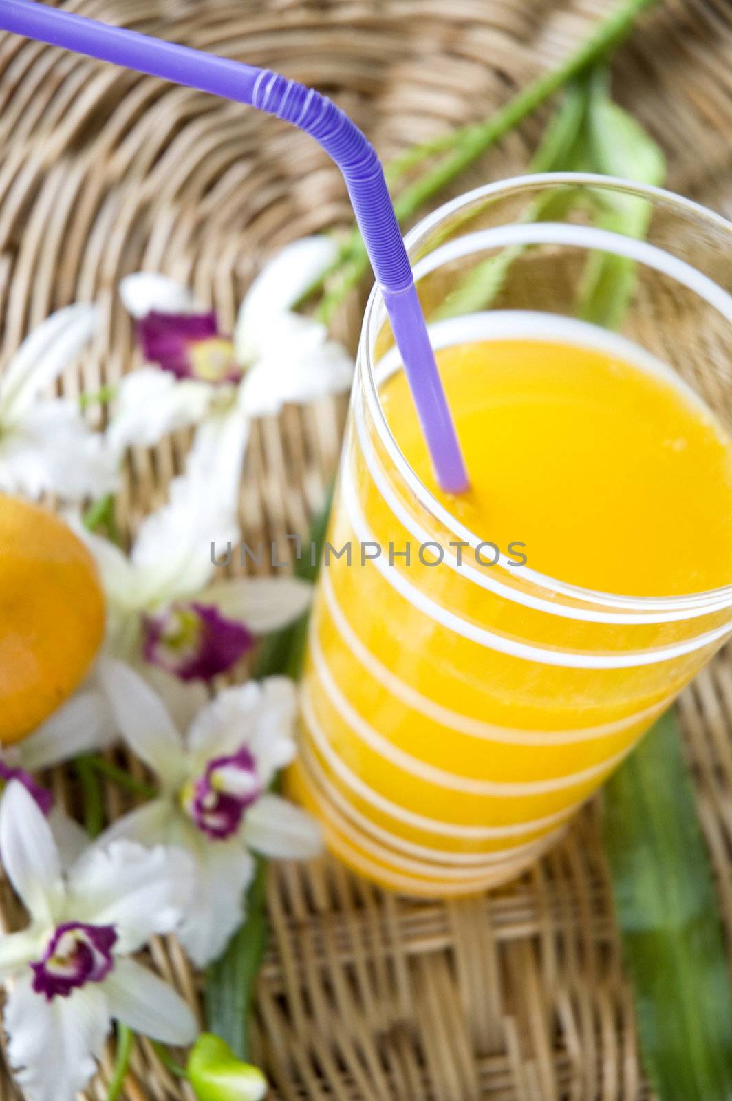 glass of orange juice with drinking straw put beside orchid