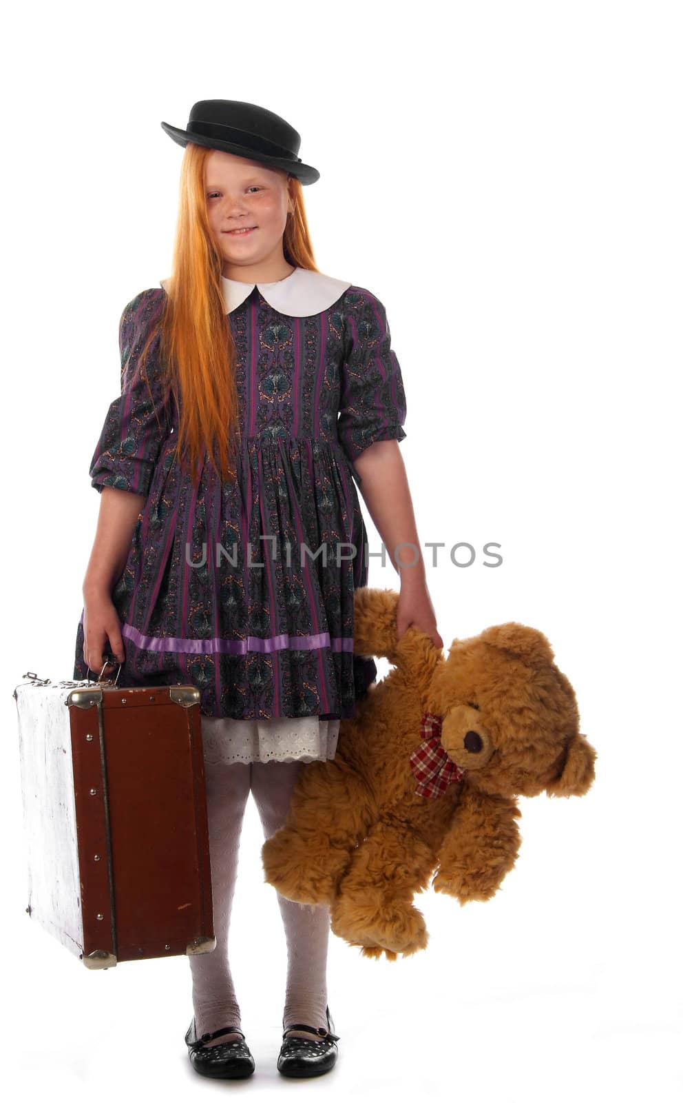 Readhead girl in an old style dress with her toy bear and trunk ready to travel