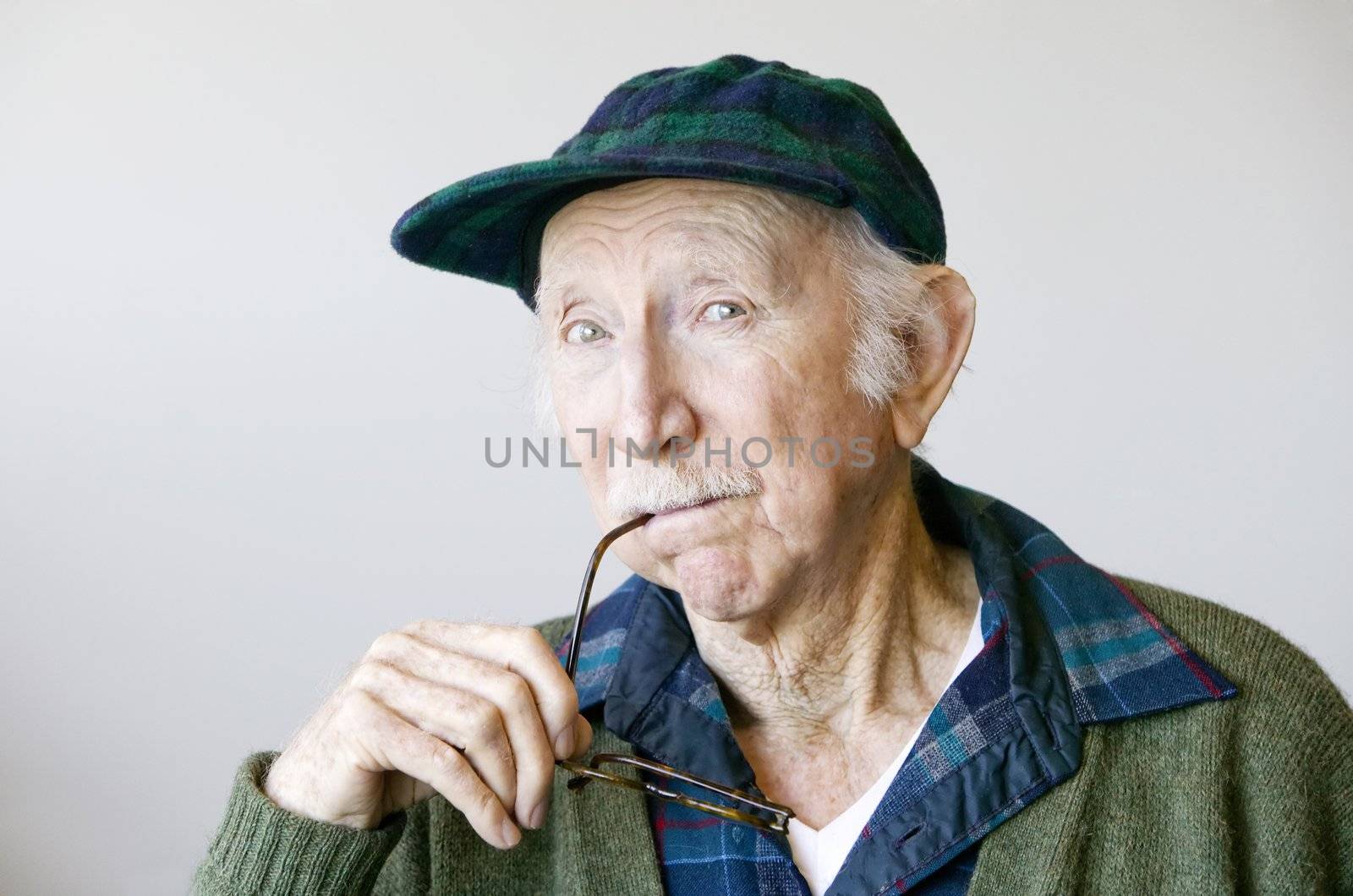 Portrait of a thoughtful senior citizen with glasses wearing a hat.