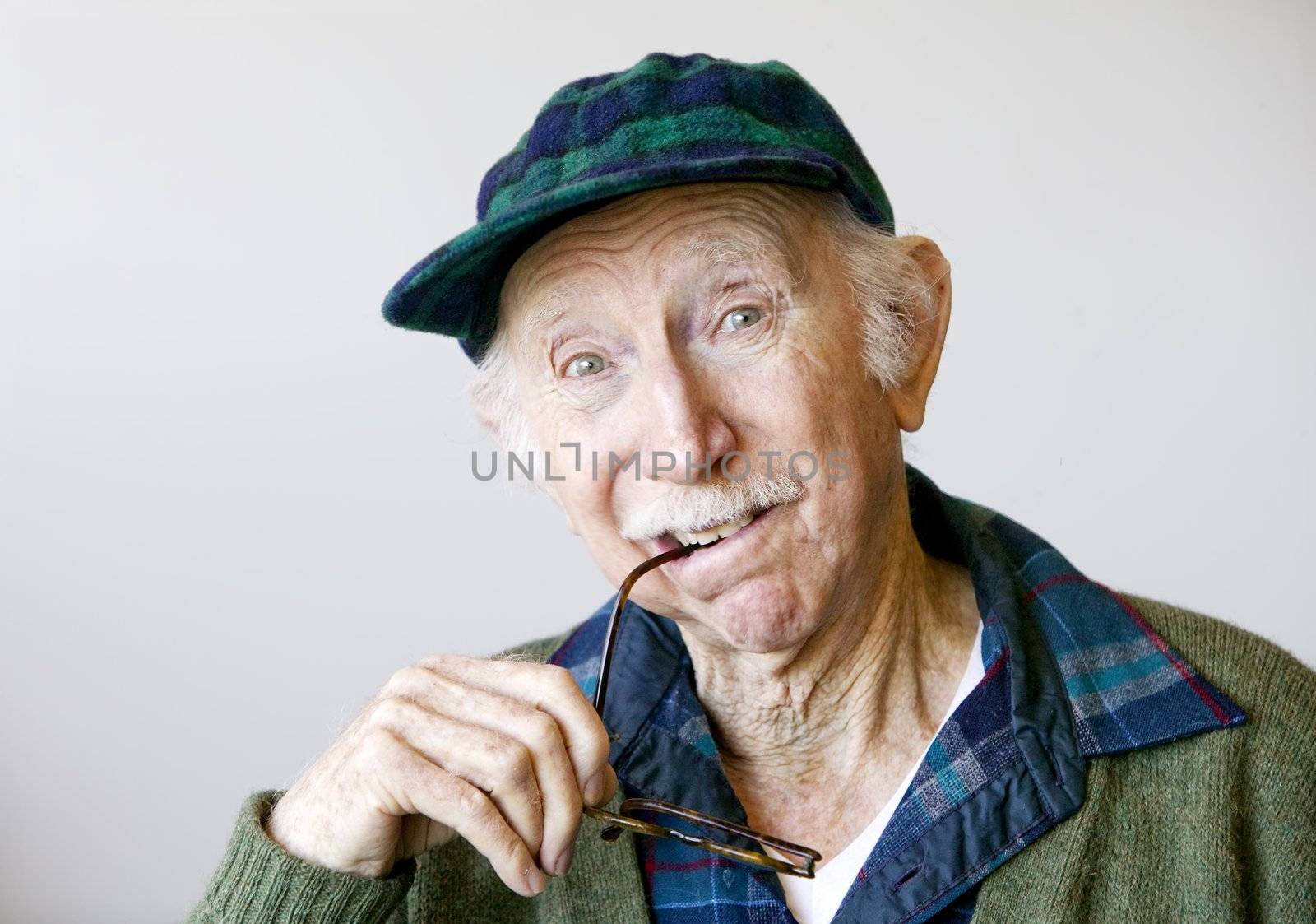 Portrait of a thoughtful senior citizen with glasses wearing a hat.