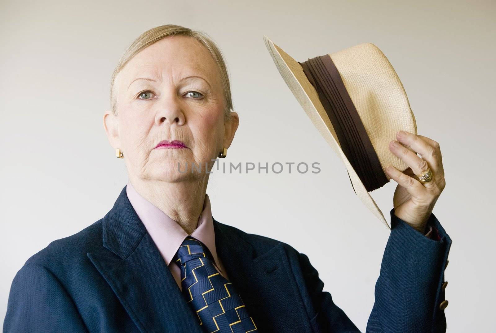 Dramatic senior woman in a man's suit holding a straw hat