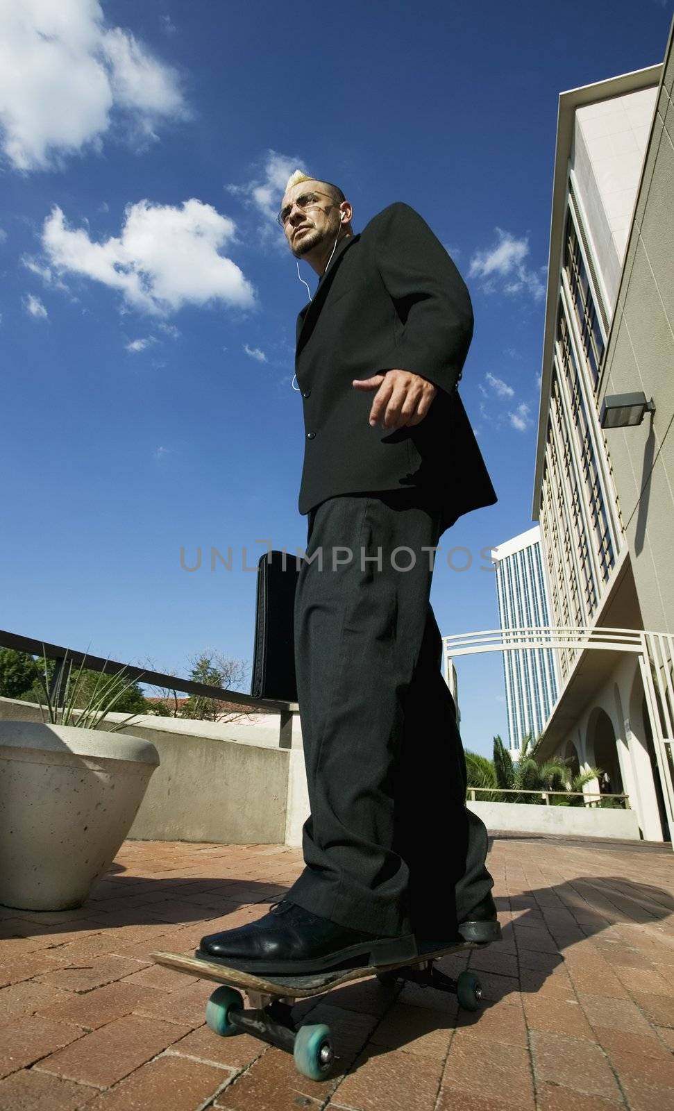 Punk businessman riding a skateboard in an office complex.