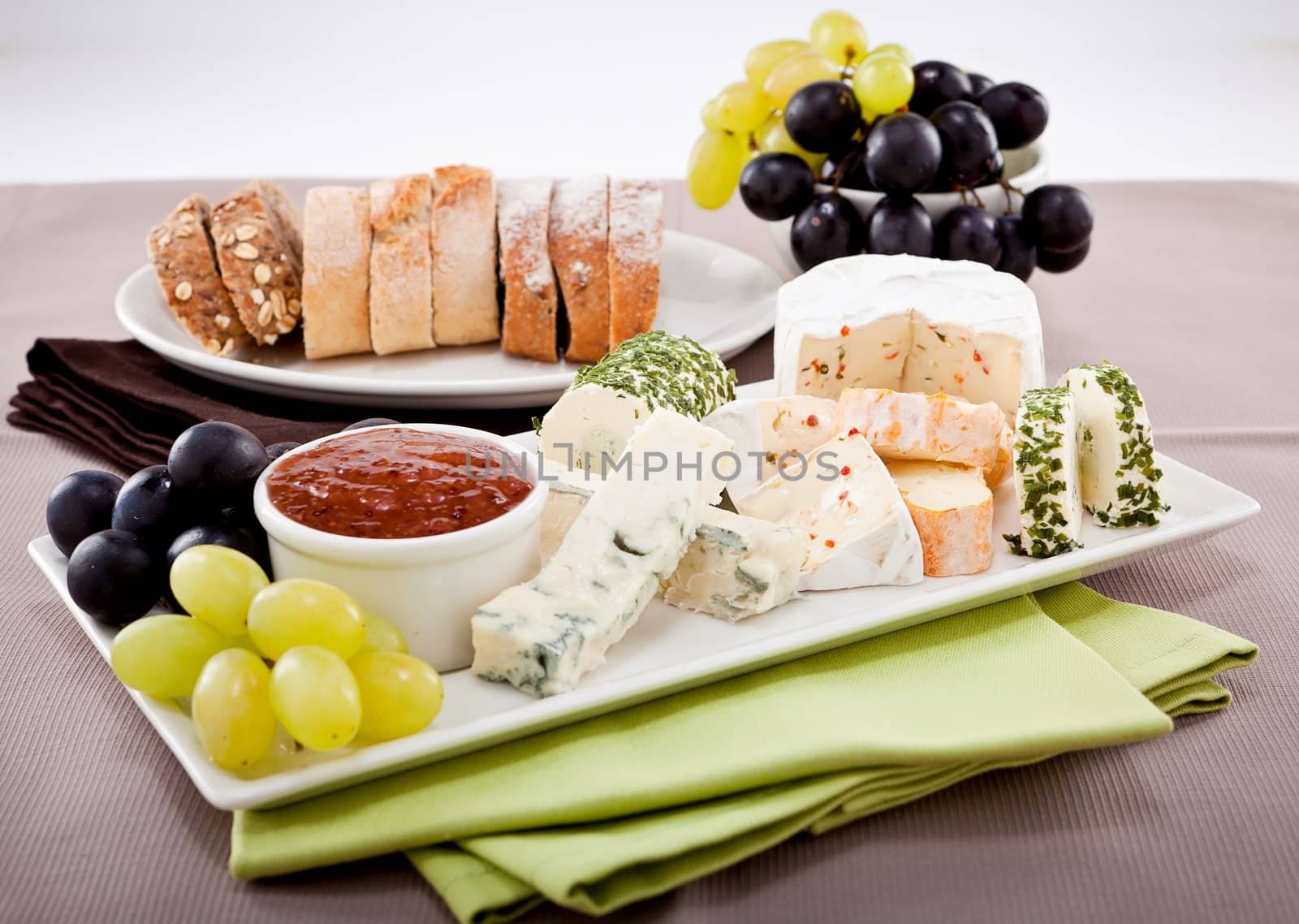 different cheese types on plate with grapes and red wine on wooden table