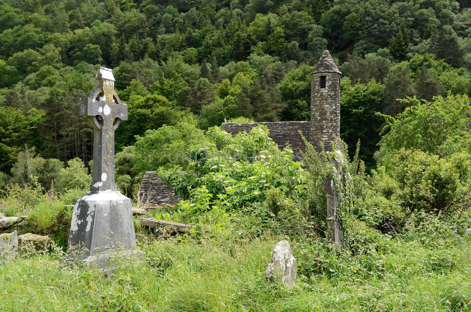 A celtic cross on the overgrown graveyard next to the medieval church of St. Kevin at the monastic heritage site Glendalough, south of Dublin in Ireland.