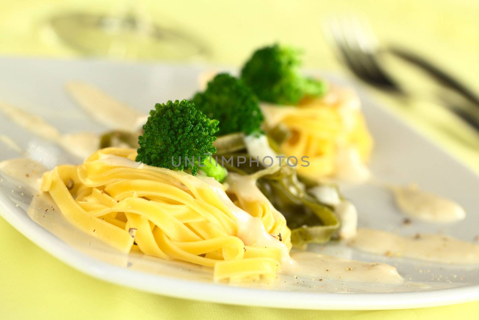 Broccoli florets on yellow and green fettuccine with bechamel sauce and ground pepper (Selective Focus, Focus on the front of the first broccoli floret)