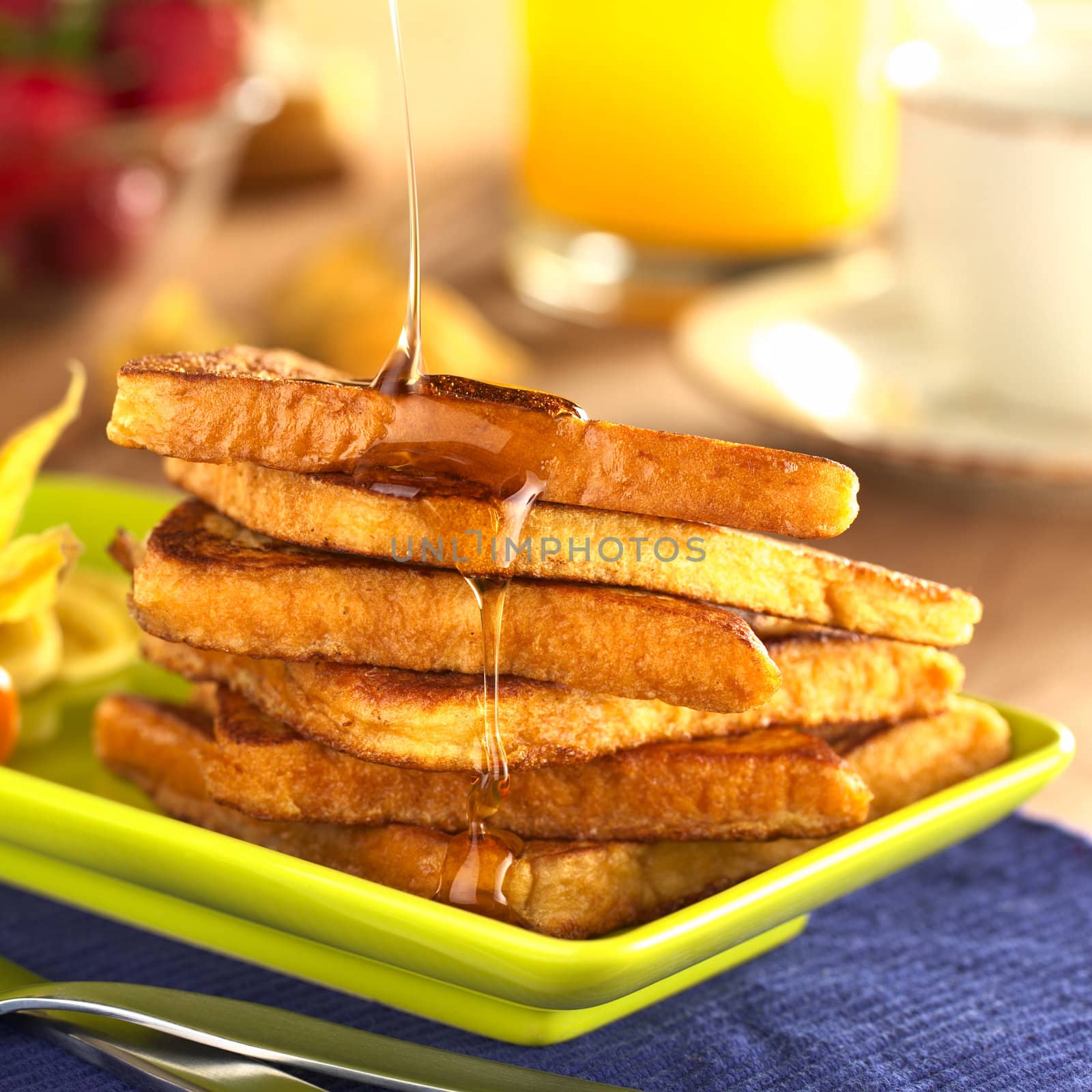 Pouring maple syrup on French toast (Selective Focus, Focus on the front of the upper slice and the syrup running down) 