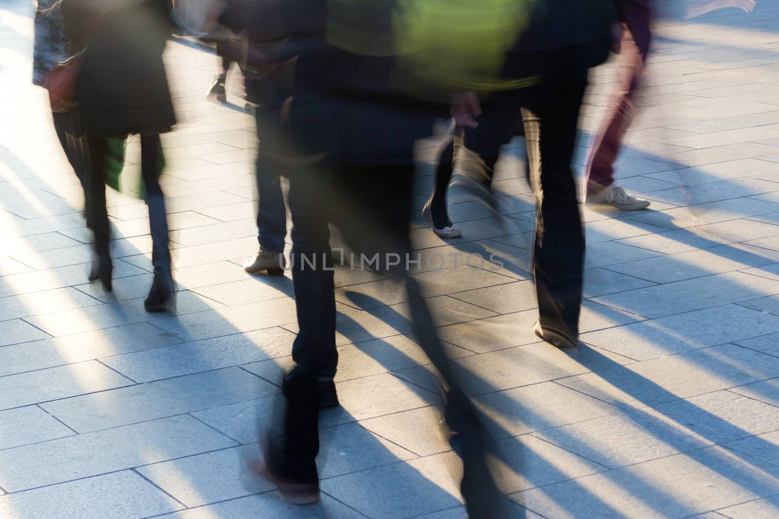 Pedestrians go towards the setting sun, to throw them on the sidewalk long shadows. Frame shot with a long exposure, motion blurred