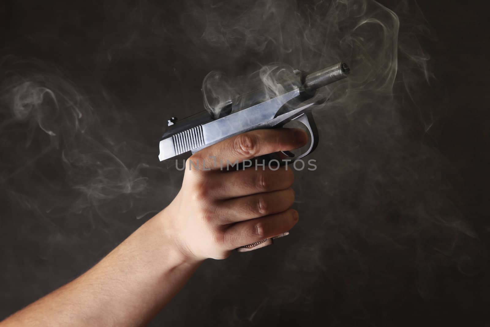 Man's hand a pistol on a dark background with a smoke