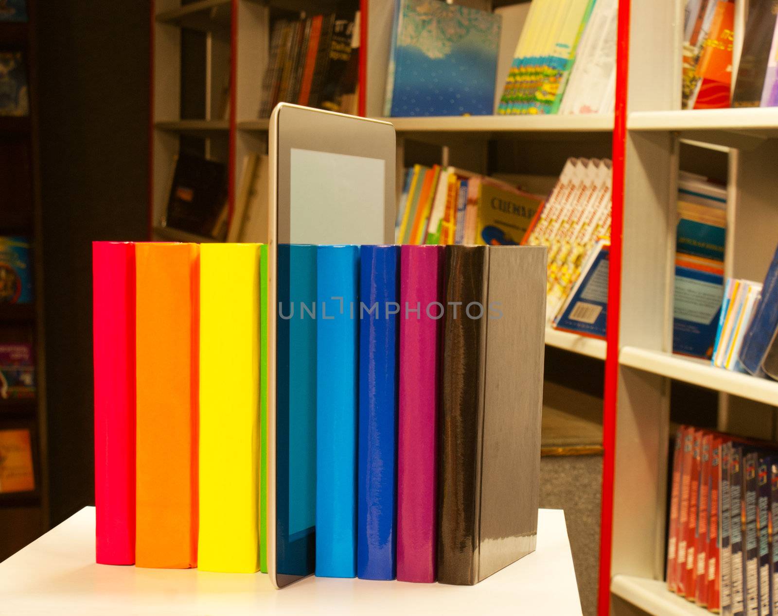 Row of colorful books and tablet PC reader in the book shop by AndreyKr