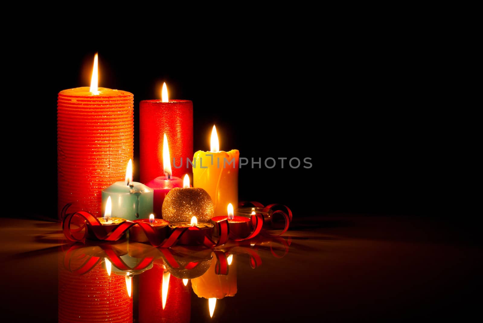 A lot of burning colorful candles against black background