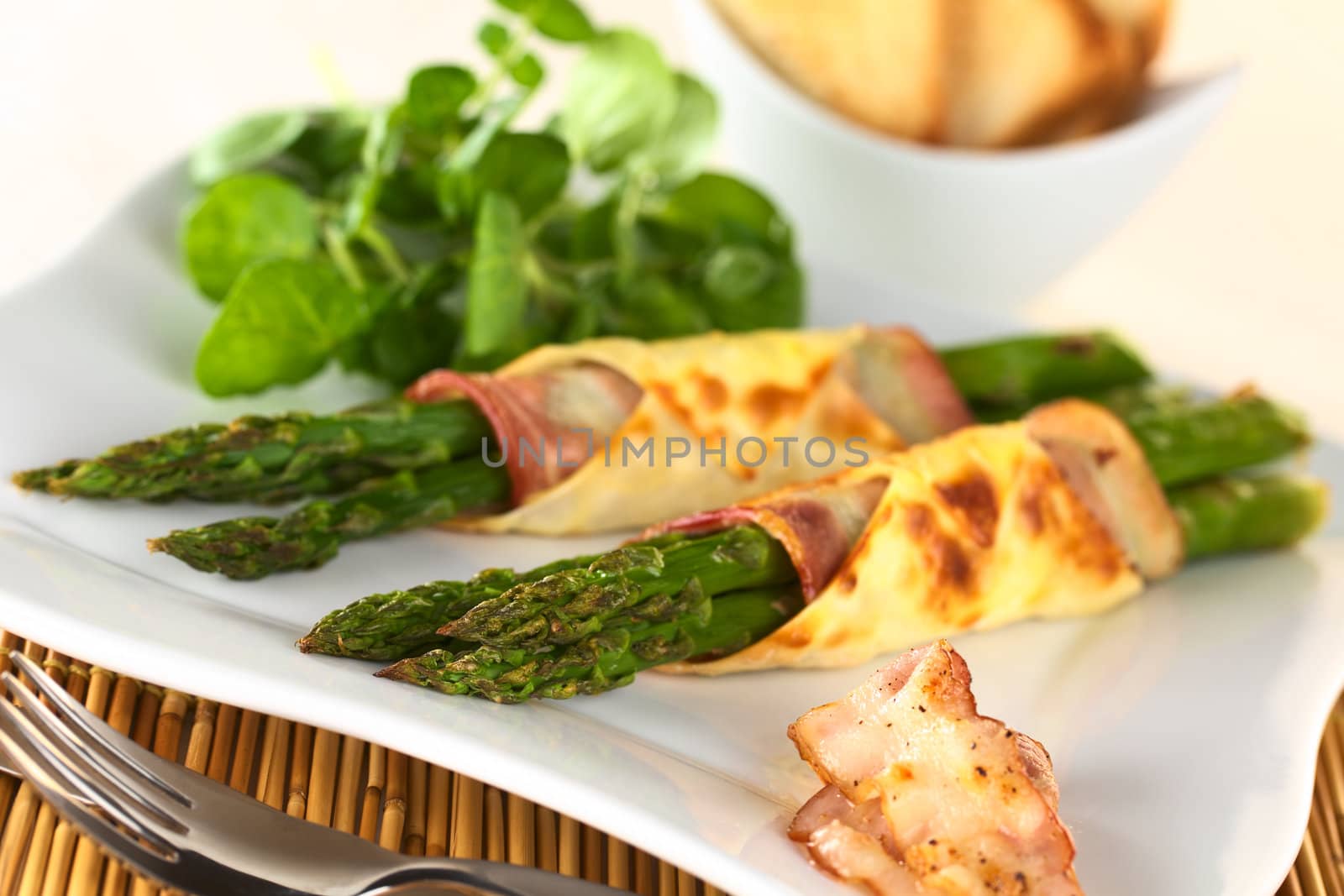 Baked green asparagus wrapped in bacon and wonton dough (Selective Focus, Focus on the asparagus tips of the first bundle)