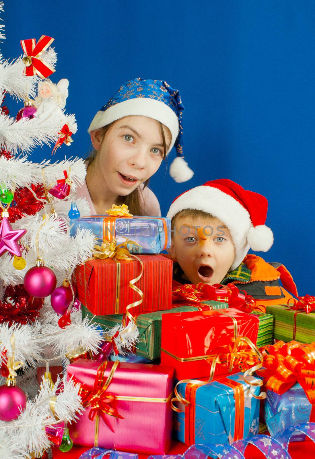 Two surprised kids looking from behind the Christmas presents