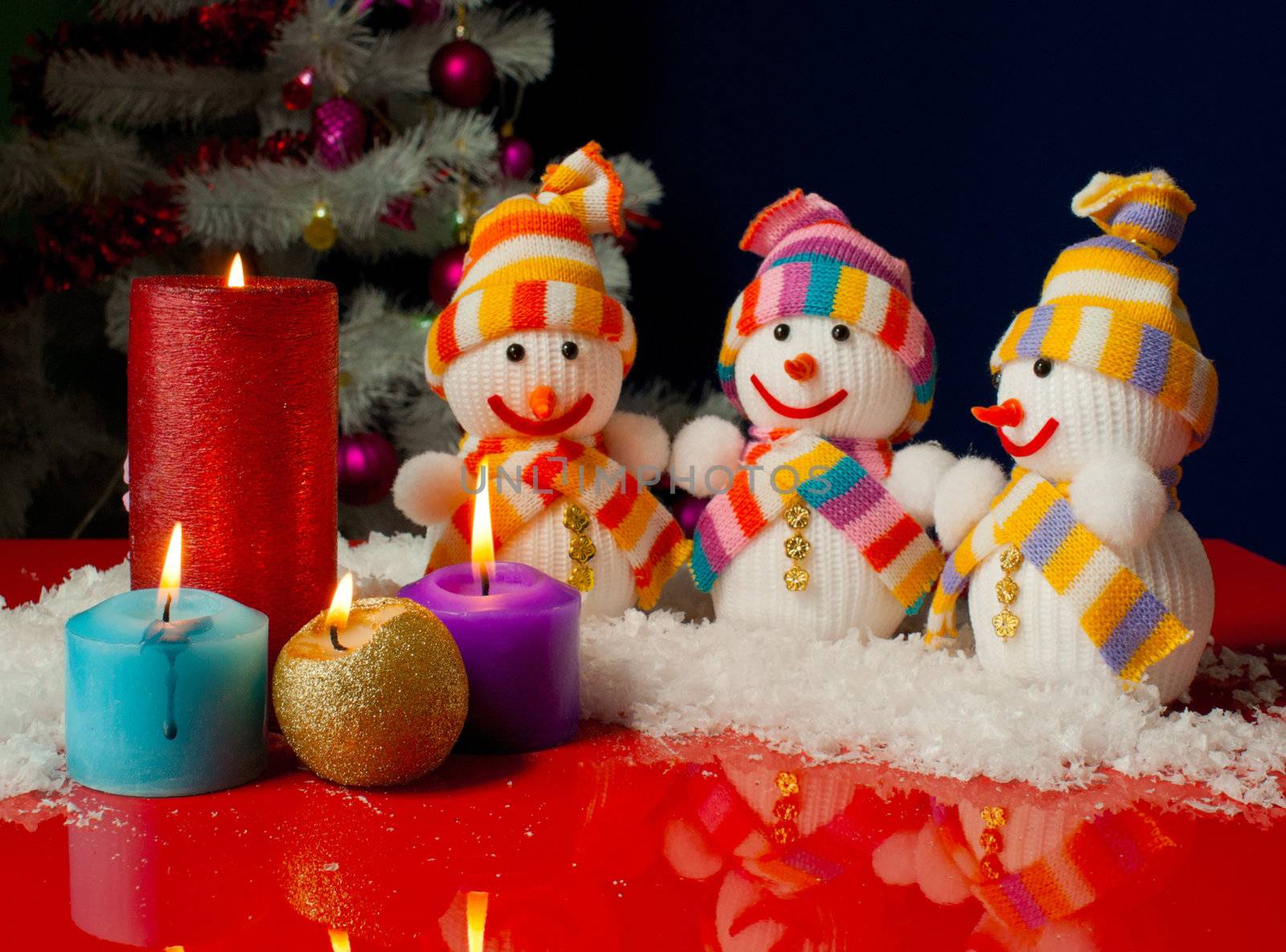 Three snowmen and burning candles over the blue background