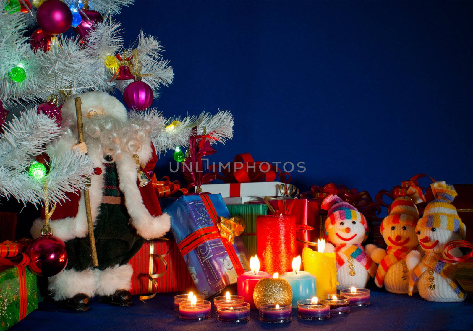 Three snowmen in front of the Christmas presents and burning candles