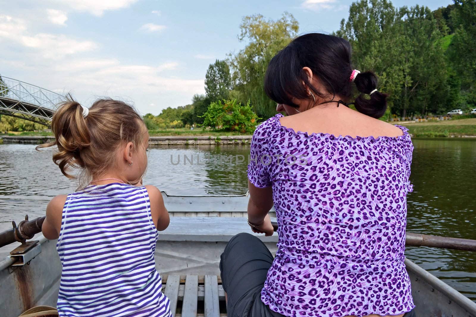 Preschooler girl and her mother ride together in a rowboat on a small fishing lake.