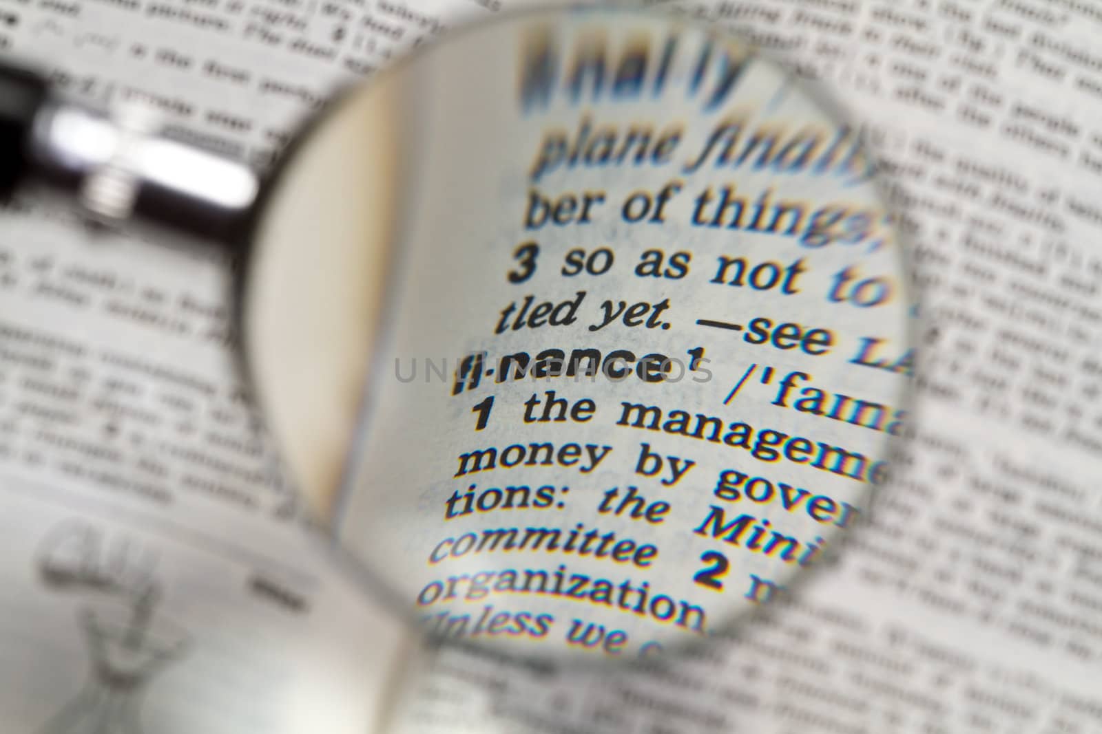 the word finance in dictionary magnified by handheld magnifying glass