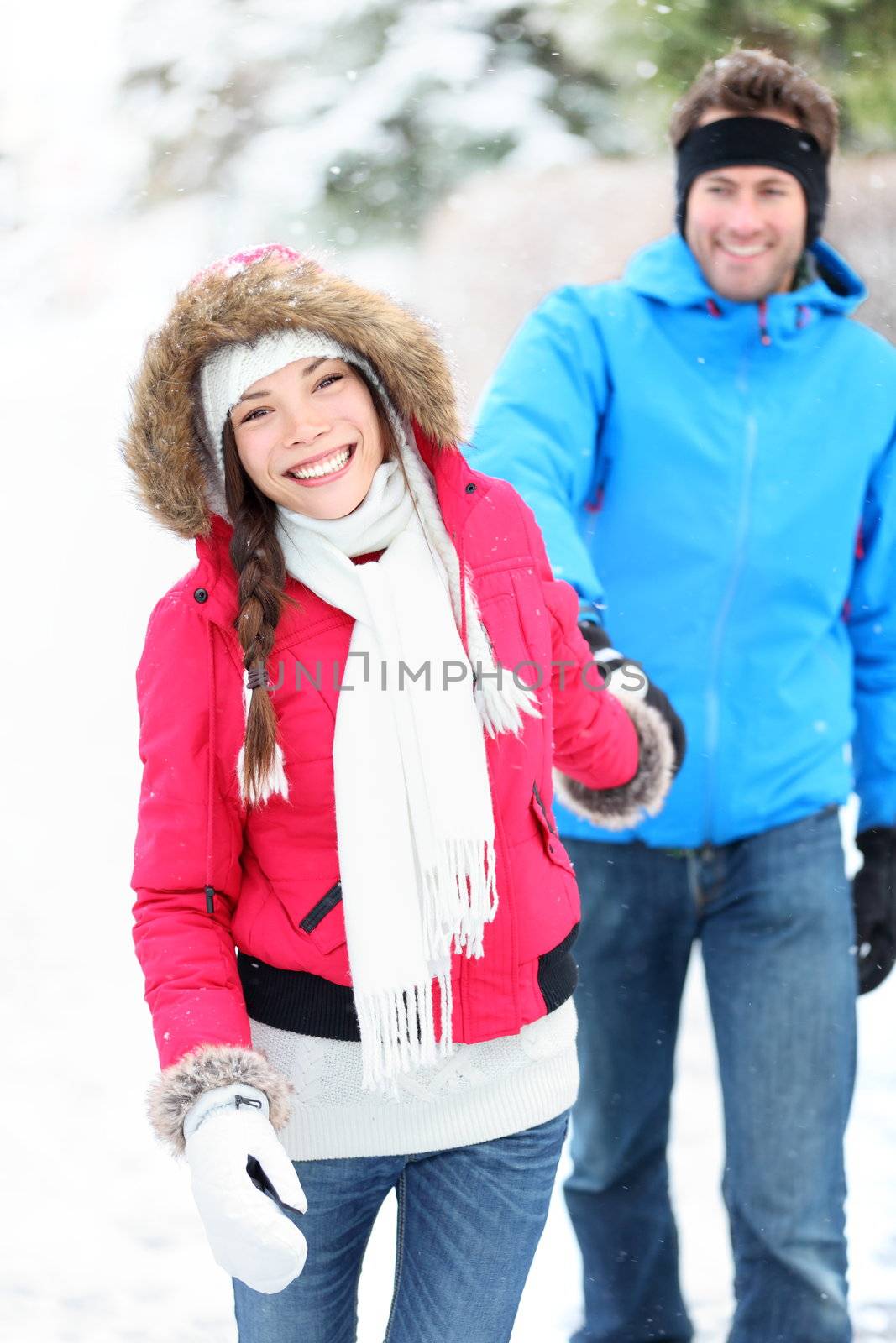 Happy winter couple walking outdoor in snow smiling happy. Beautiful young multi-racial couple, Asian woman, Caucasian man.