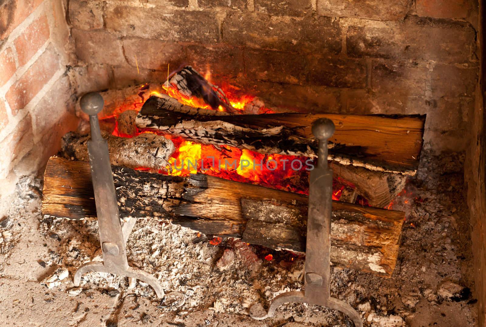 Ancient brick fireplace with wooden logs smouldering