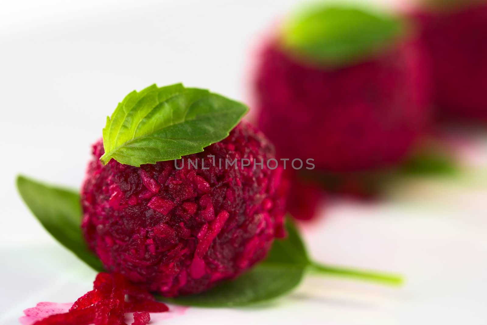 Beetroot coconut balls garnished with basil leaves (Selective Focus, Focus on the front of the first ball and the front of the basil leaf on top)