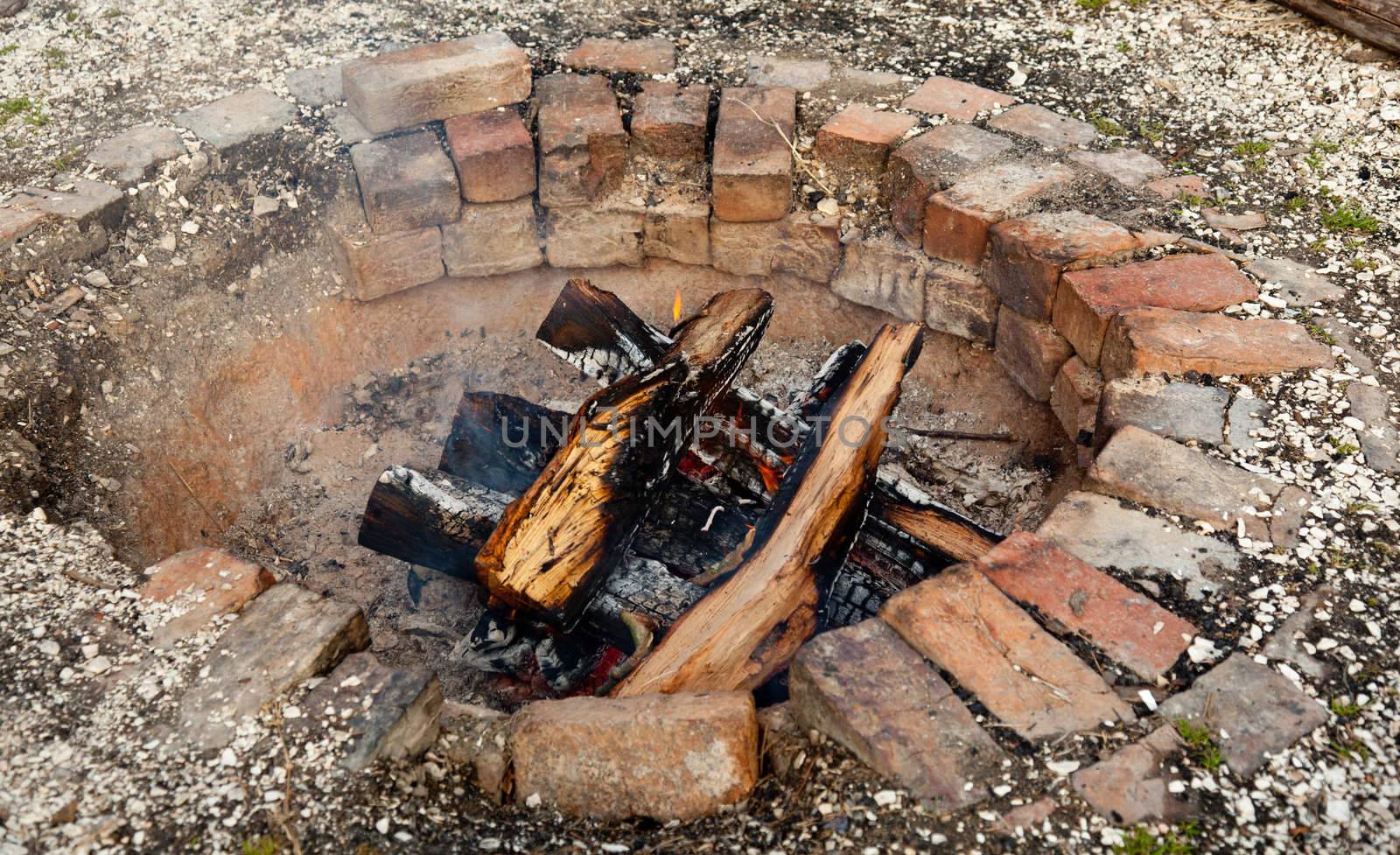 Ancient brick firepit with wooden logs smouldering