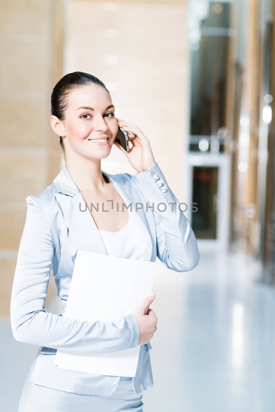 Portrait of a successful business woman in the office, holding papers and talking on cell phone