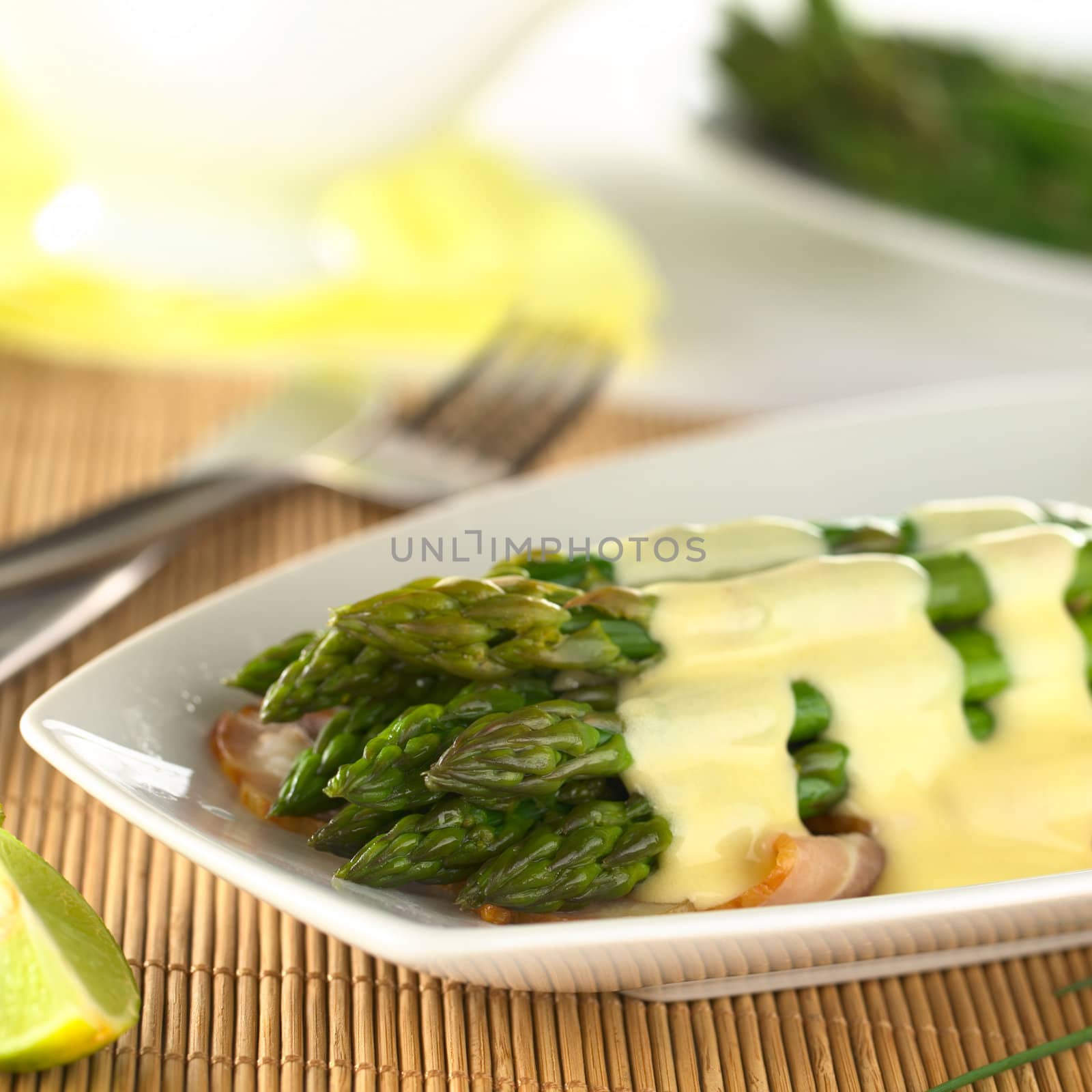 Cooked green asparagus on fried bacon with Hollandaise sauce on top (Selective Focus, Focus on the three asparagus tips in the front)